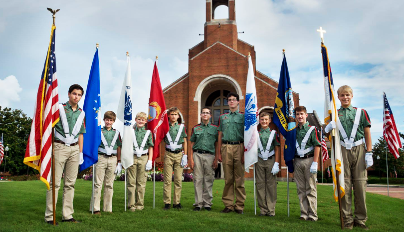 Girl Scouts standing in uniform holding various flags outside a church.