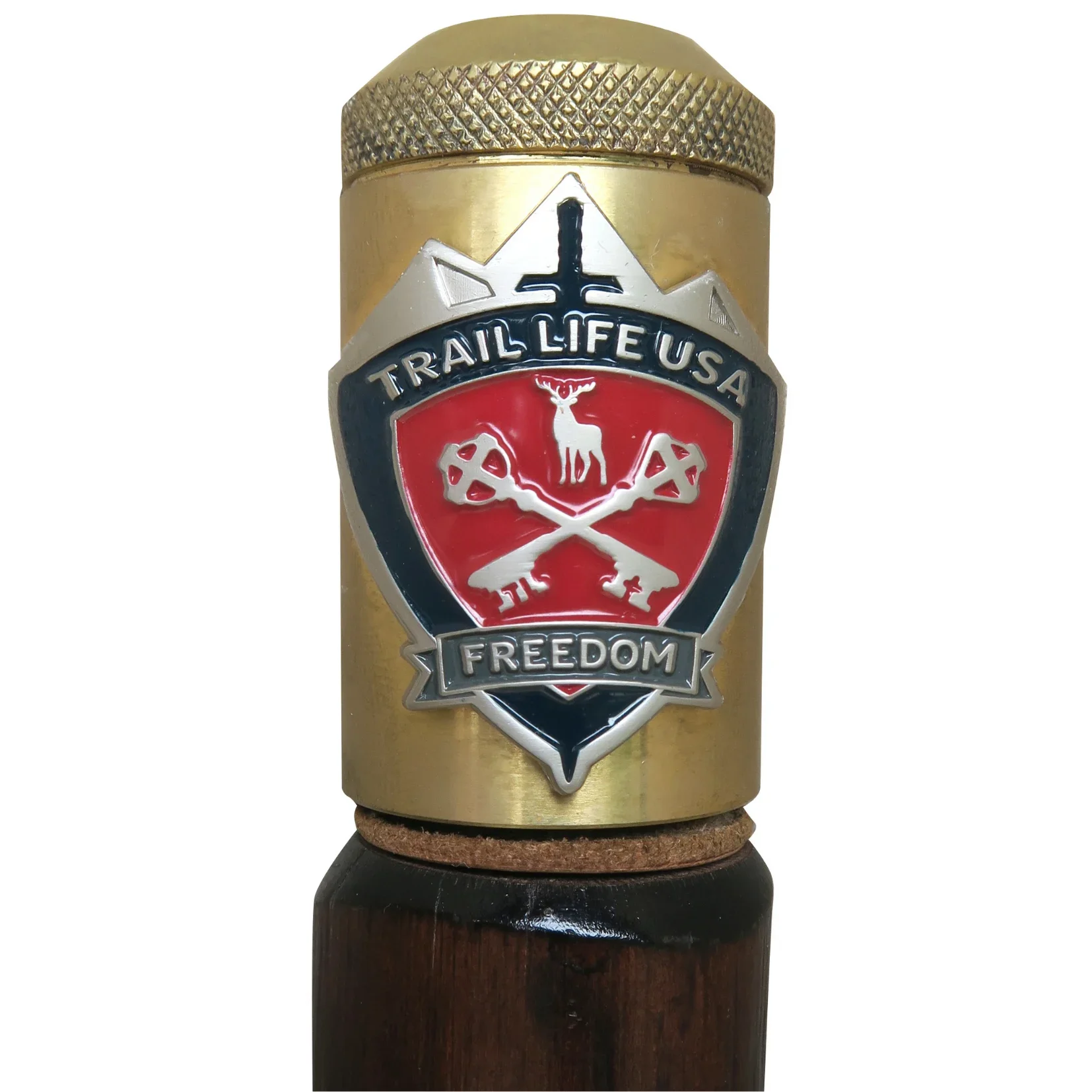 Close-up of a metal badge attached to a gold-colored cylindrical object, featuring a mountain, a deer, crossed keys, and the words 'Trail Life USA' and 'Freedom'.