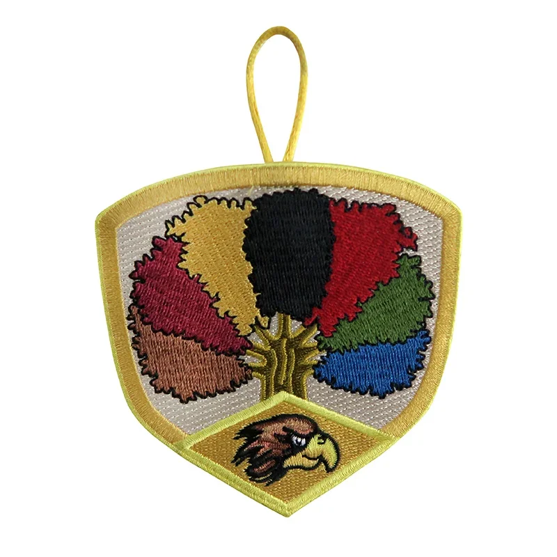 An embroidered patch featuring a shield shape with a tree with multicolored leaves and an eagle head at the bottom.