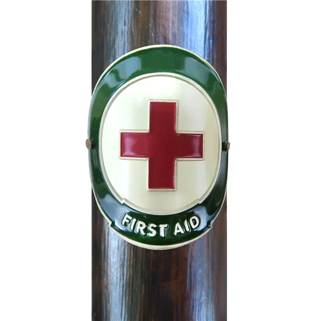 Vintage first aid sign with a red cross and green border mounted on a wooden surface.
