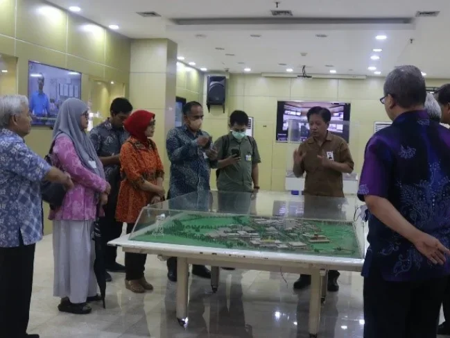 Group of people gathered around a detailed scale model of a development project displayed on a table, with a man explaining it.