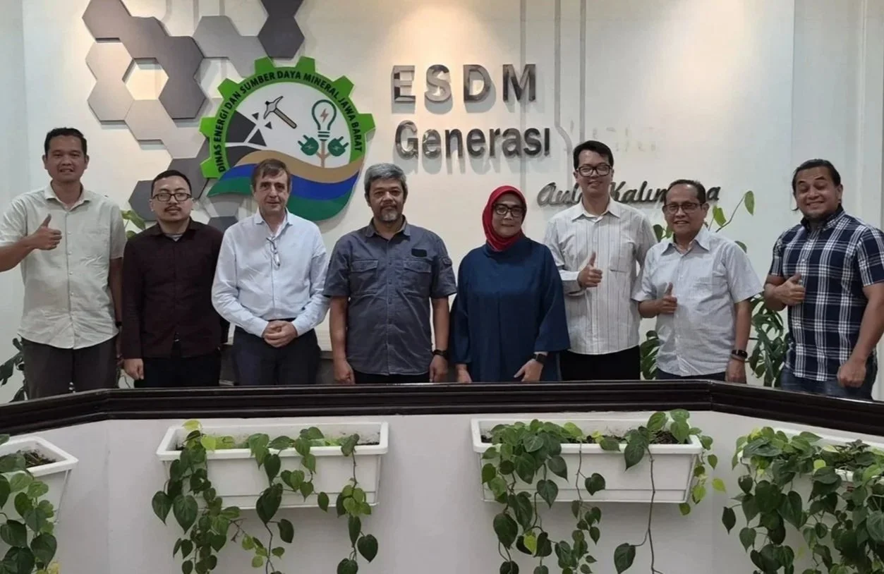 Group of nine people standing indoors in front of a wall with the logo and text 'ESDM Generasi' and 'Ali Kalim.' There are potted plants in front of them and wall decorations behind. The individuals are smiling and giving thumbs-up gestures.