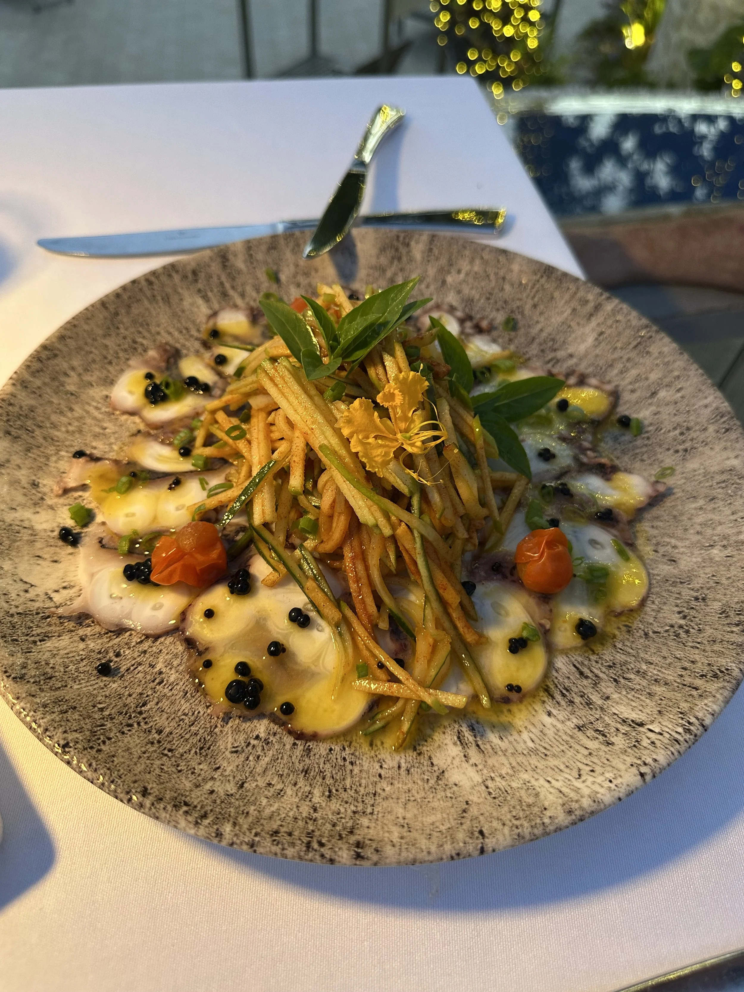 A plate of food topped with black pepper, cherry tomatoes, green herbs, and a central heap of sliced vegetables garnished with fresh basil leaves.