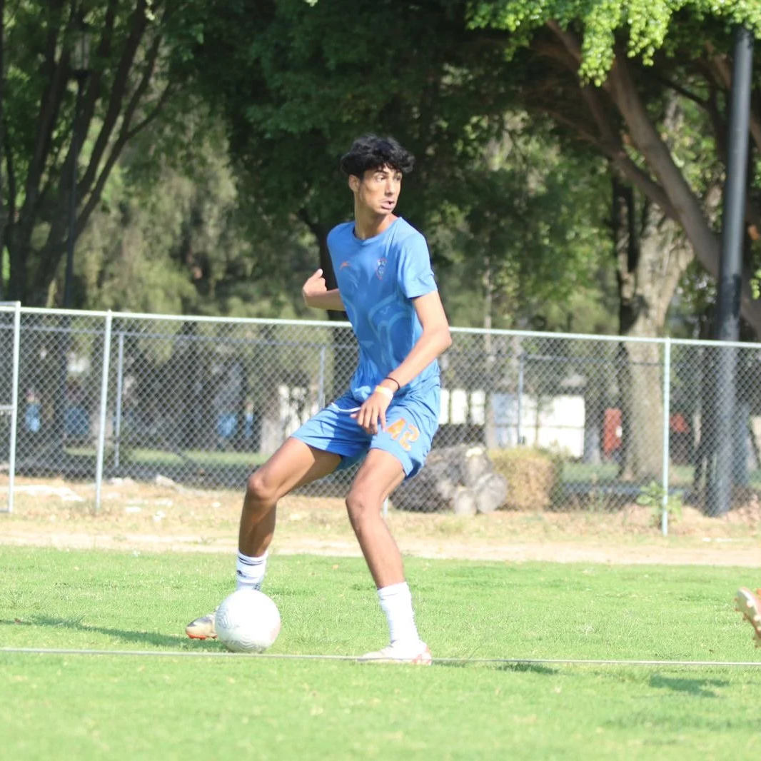 A young man in blue soccer uniform dribbling a white soccer ball on a grassy field during daytime.
