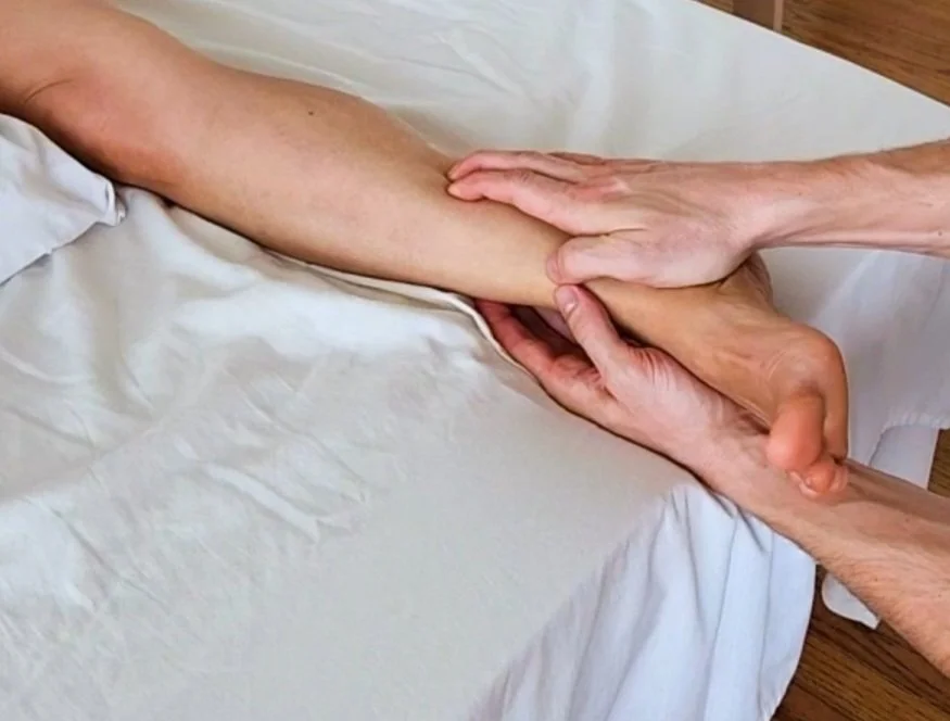 Person receiving a massage on their forearm from a massage therapist in a clinical setting.