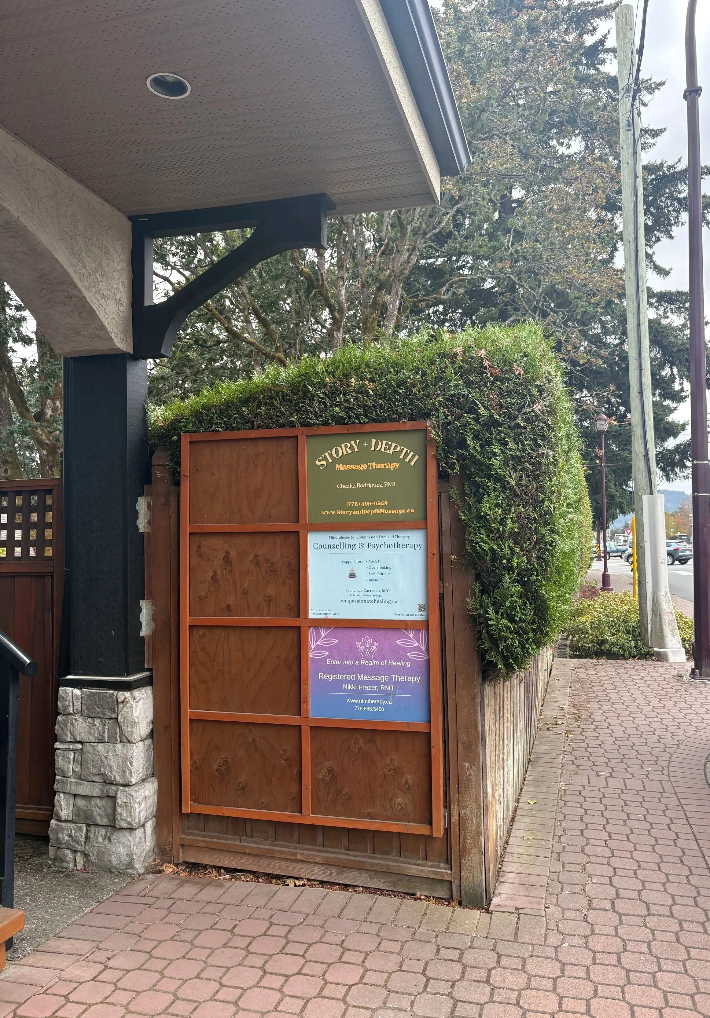 Signage for Story and Depth Massage Therapy on wooden post with signage of other nearby businesses.