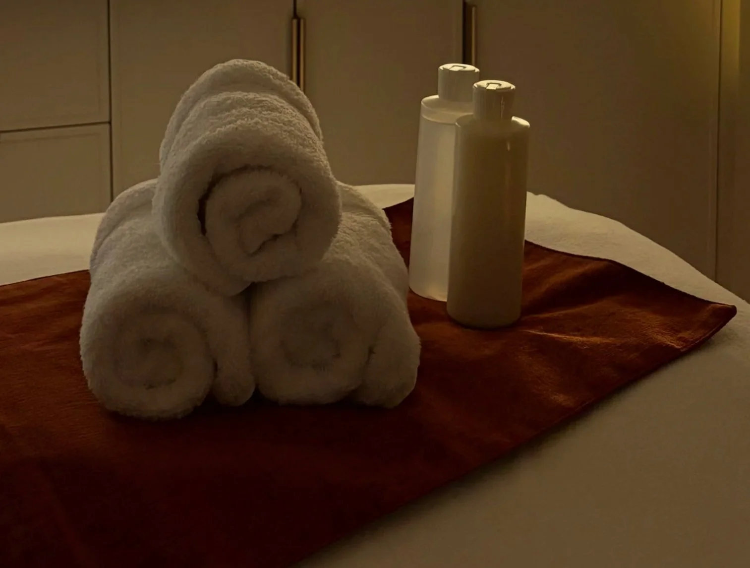 Picture neatly rolled towels beside a bottle of massage lotion and oil.