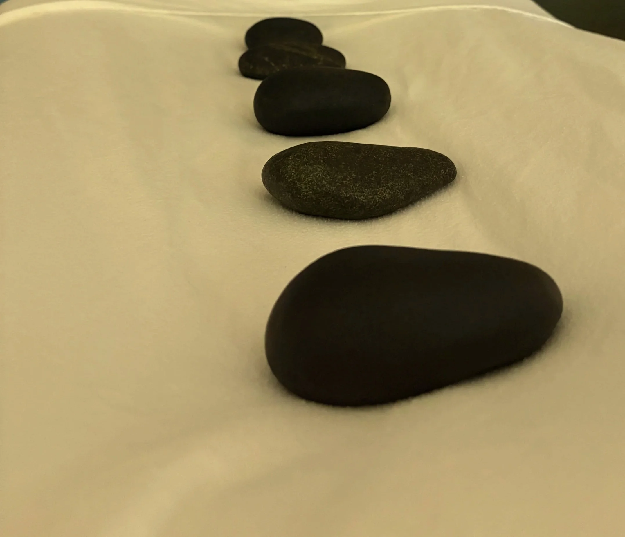 A close up of hot stones placed in a neat row on a massage table.