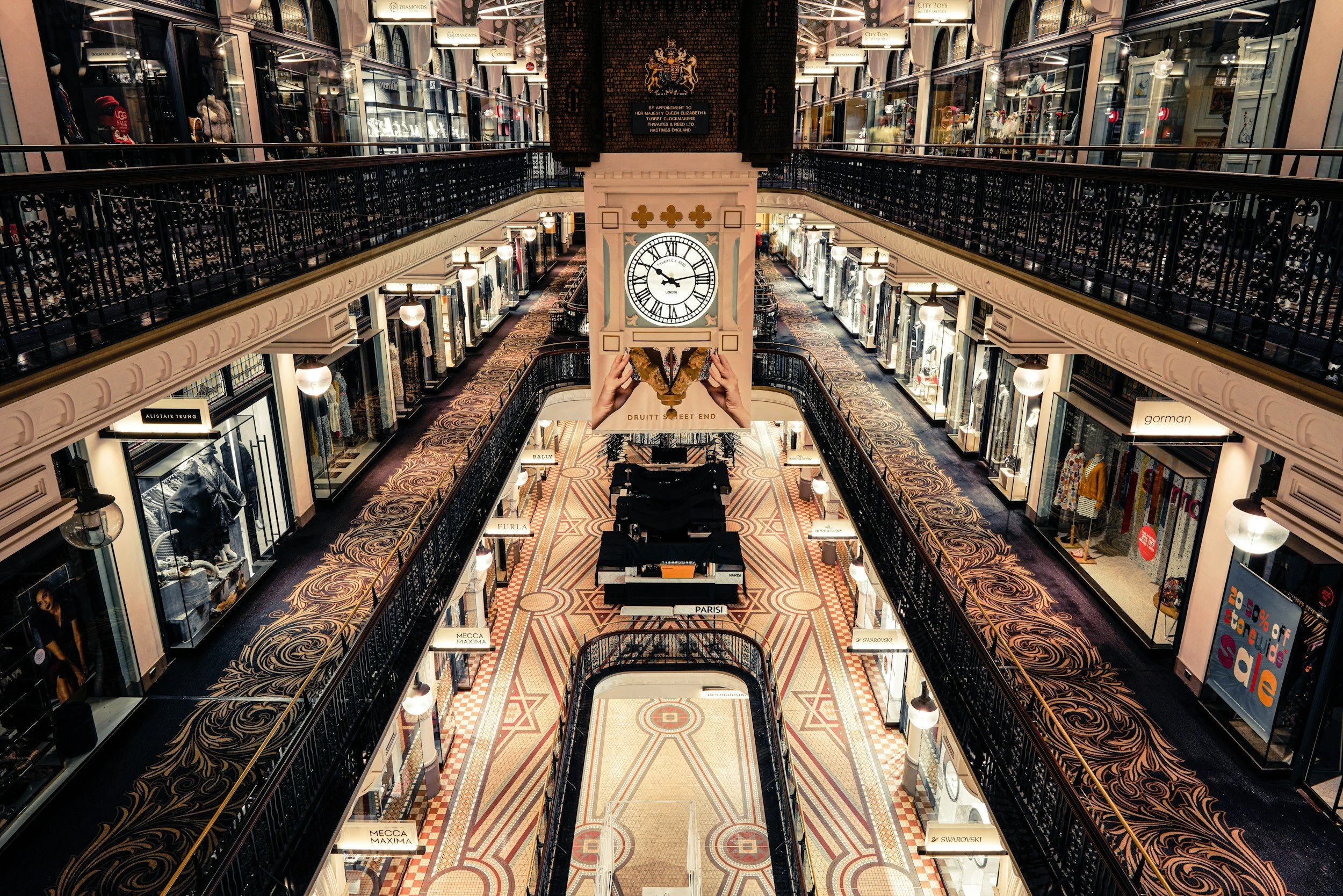 Interior of a multi-level shopping arcade with decorative railings and a hanging clock.