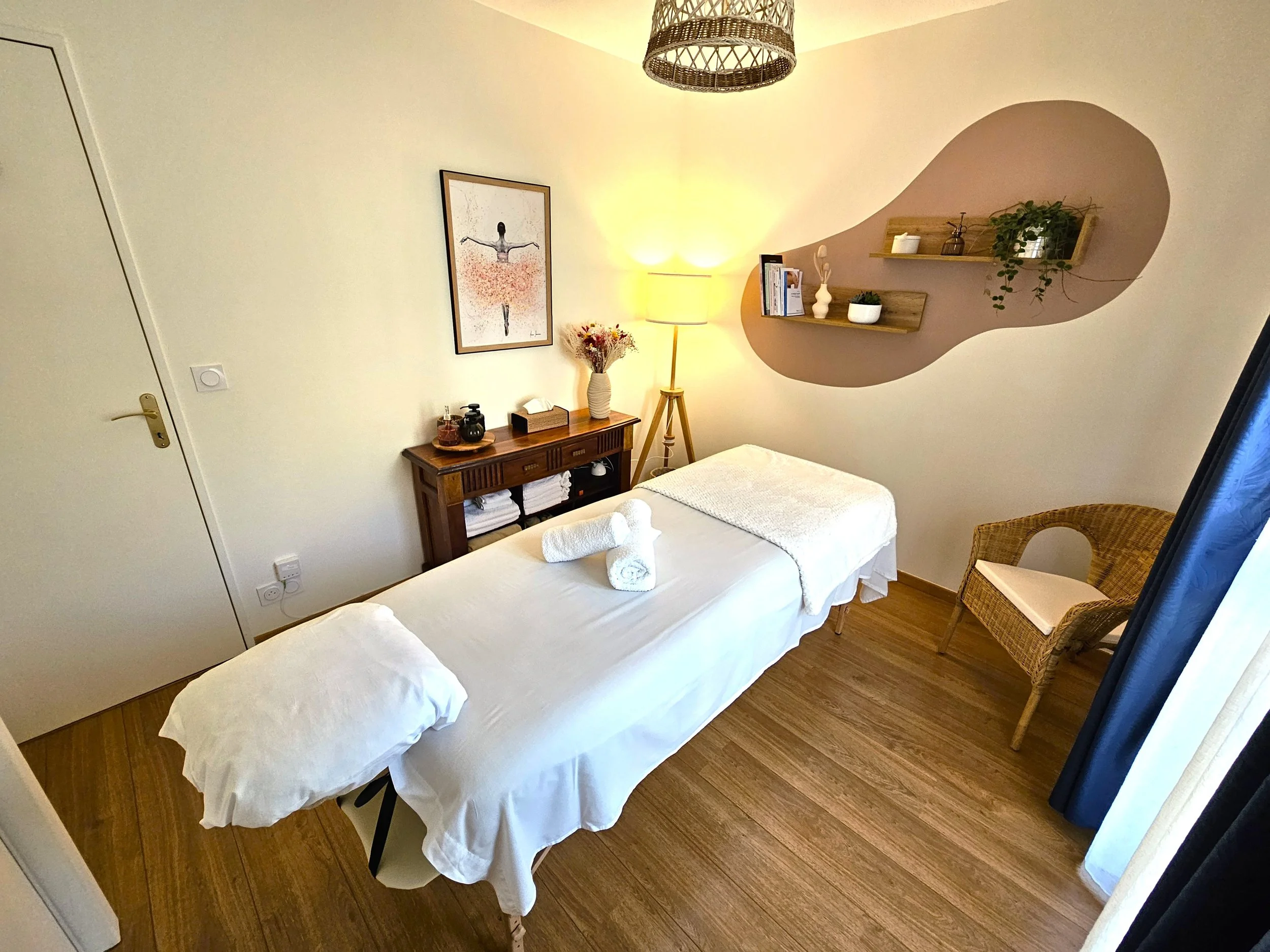 Salle de soins cosy avec des couleurs chaudes et une table de massage, drap blanc, serviettes blanches et un coussin, à Cambo-les-bains.