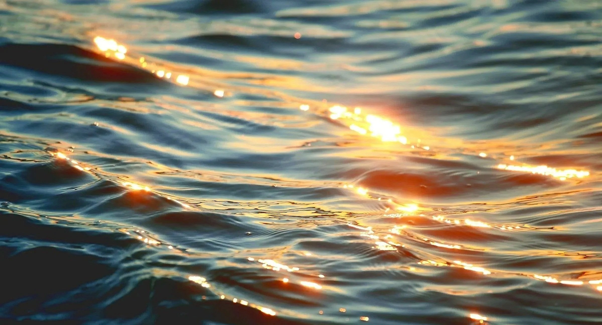Close-up of water with reflections of sunlight creating shimmering, golden highlights on the surface.