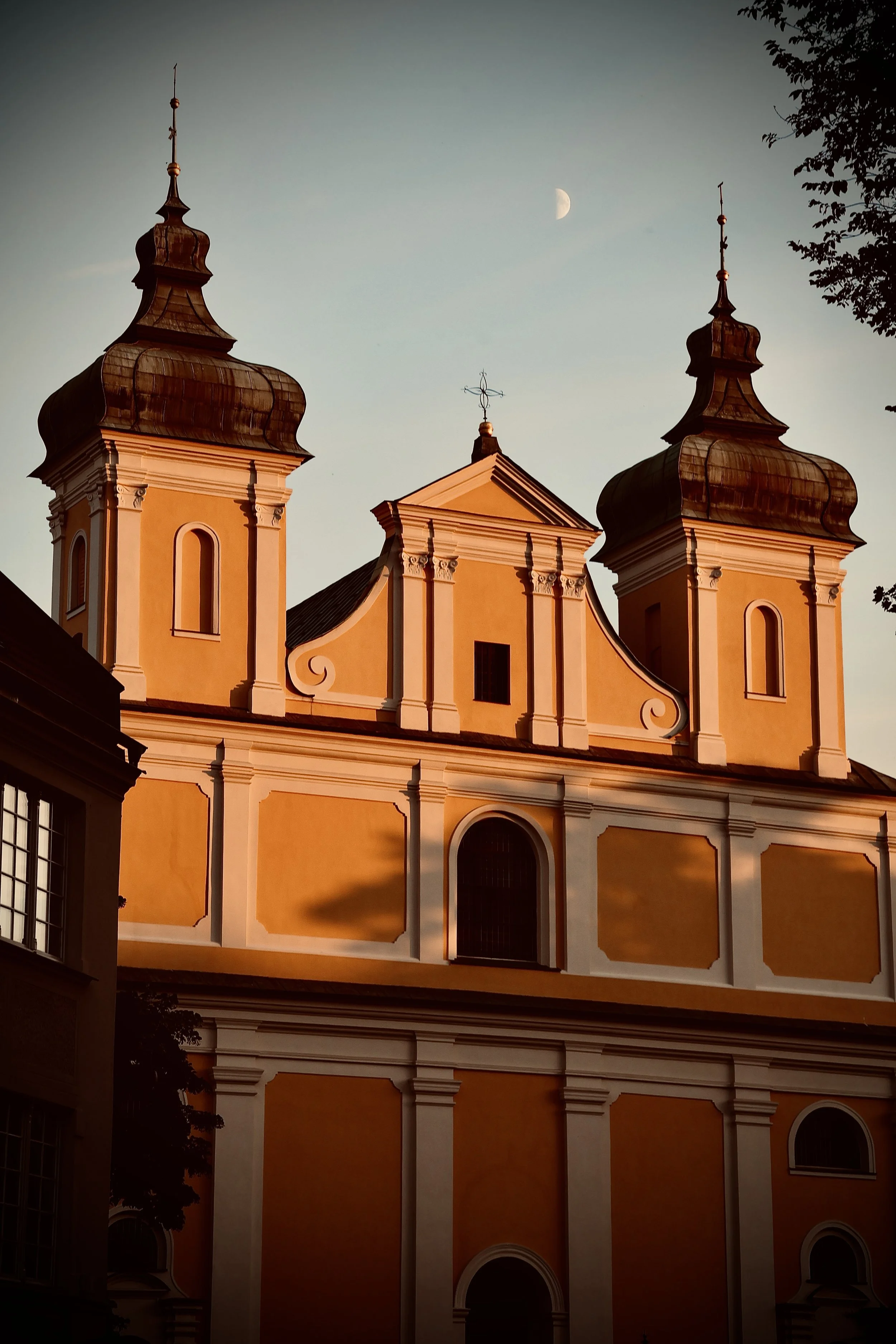 The image shows a historic church building with two steeples, painted in warm yellow and white tones. The sky above features the moon.
