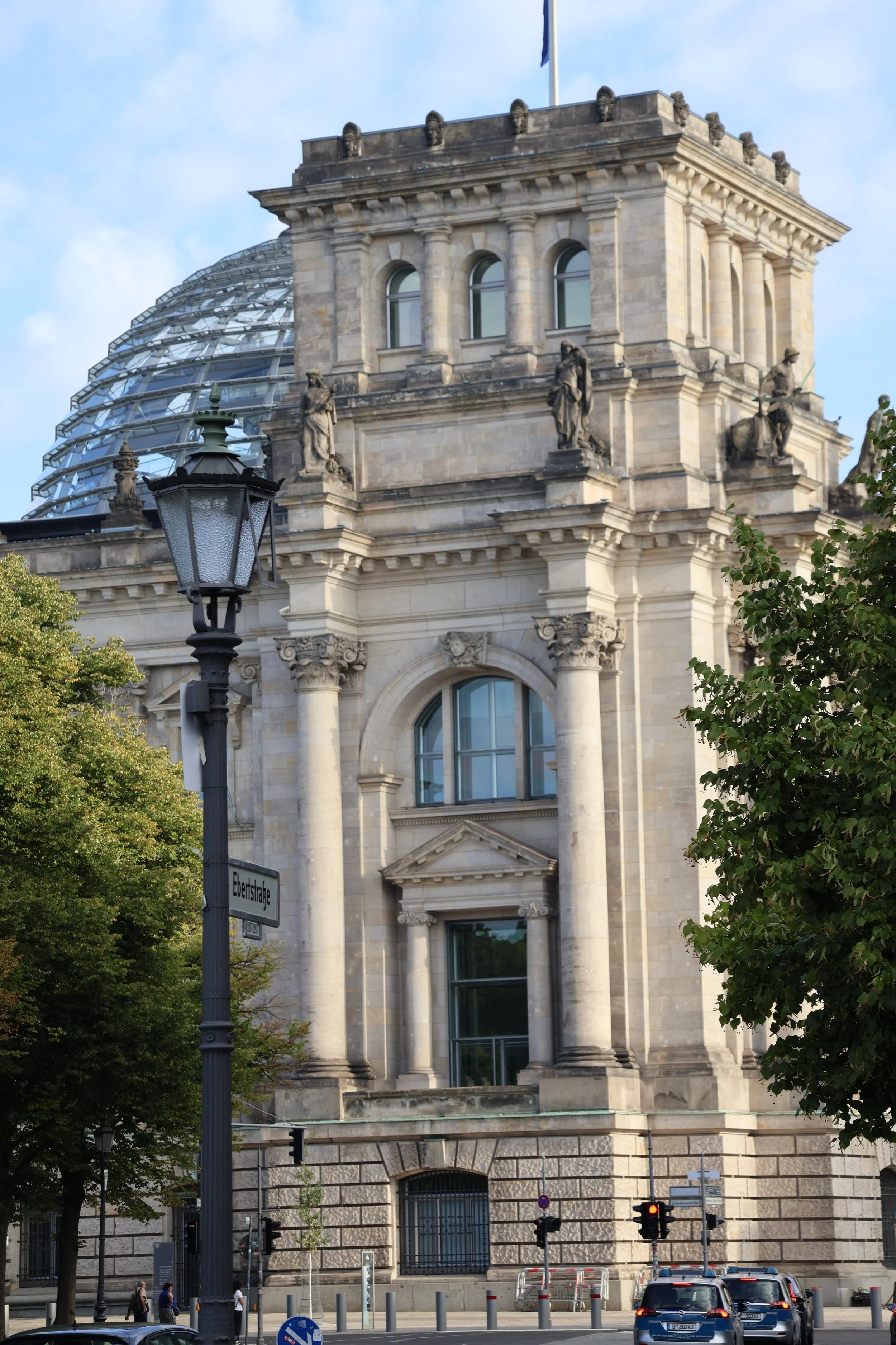 Historical building with classical architecture, statues, and a glass dome in the background. A street scene with cars, traffic lights, and pedestrians.