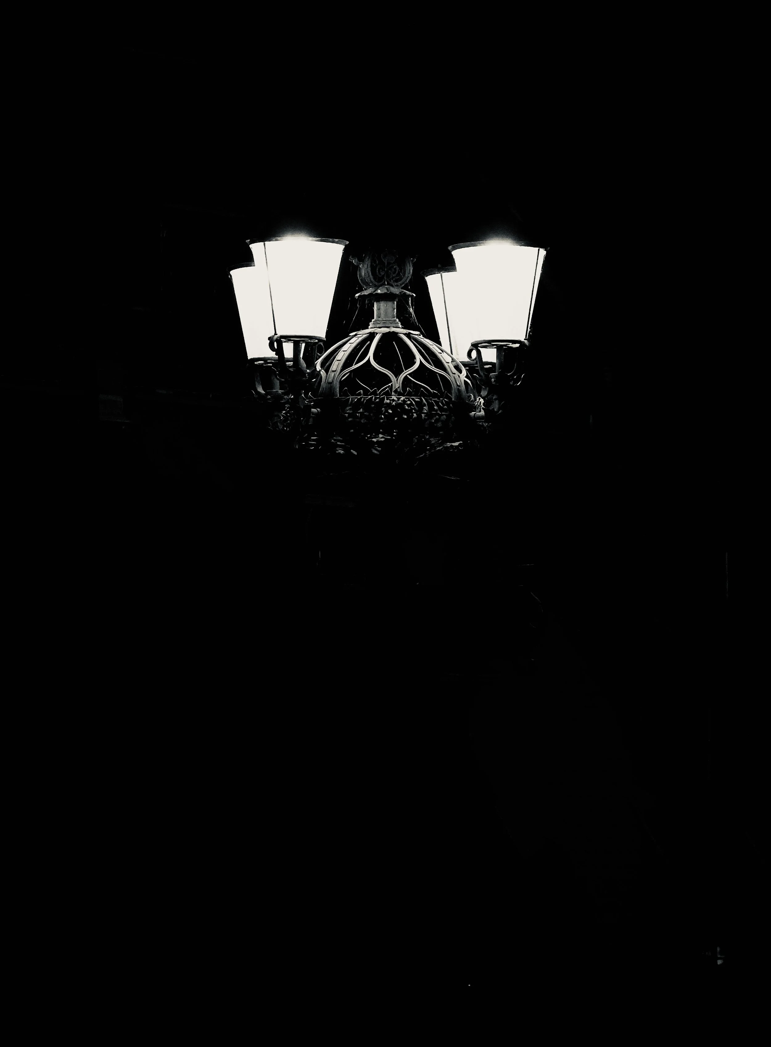 A black chandelier with white lampshades and intricate metalwork details, mounted on a dark ceiling.