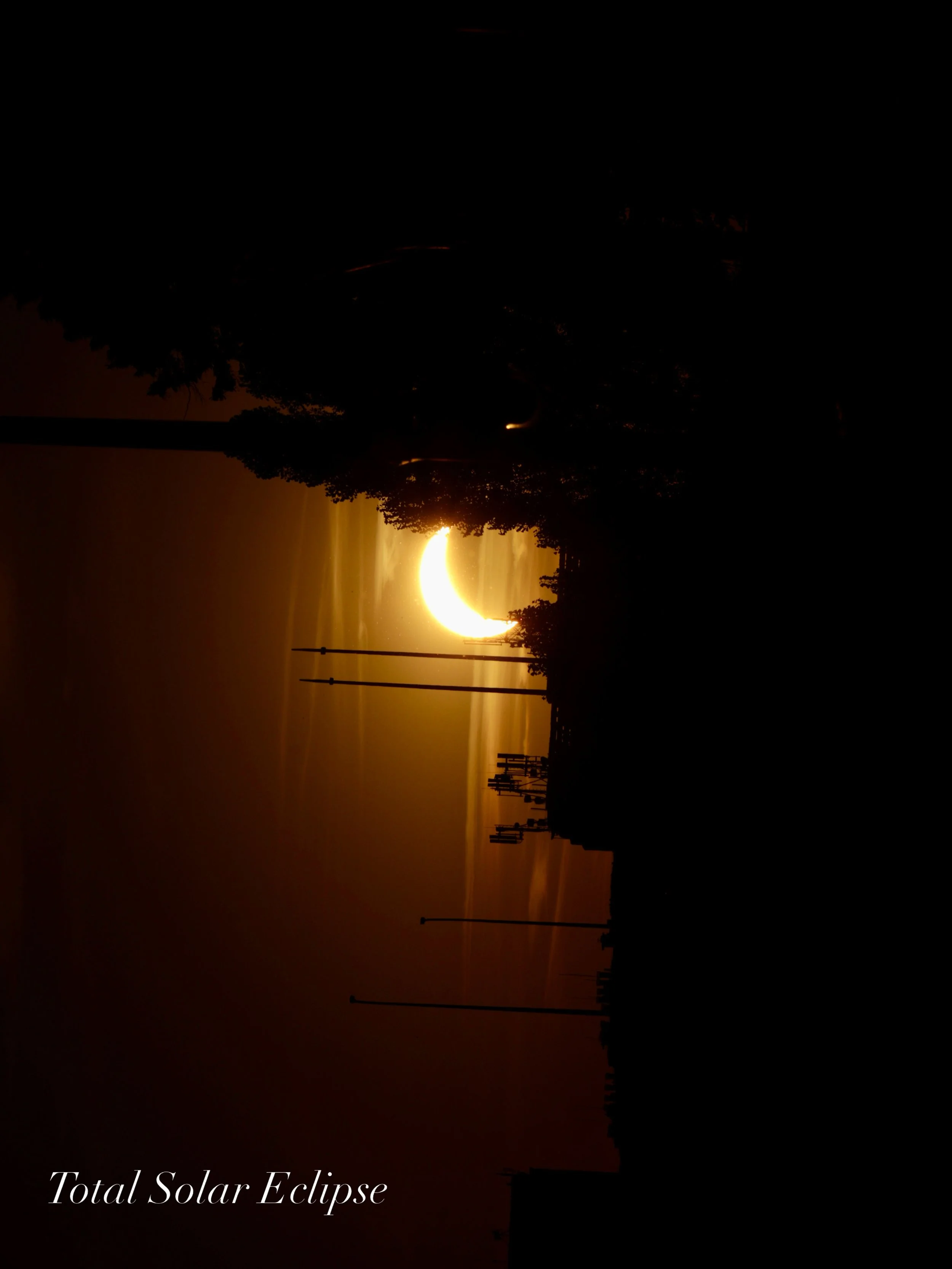 A total solar eclipse occurring over a city skyline at sunset, with the moon covering the sun and casting a dark shadow over the scene.