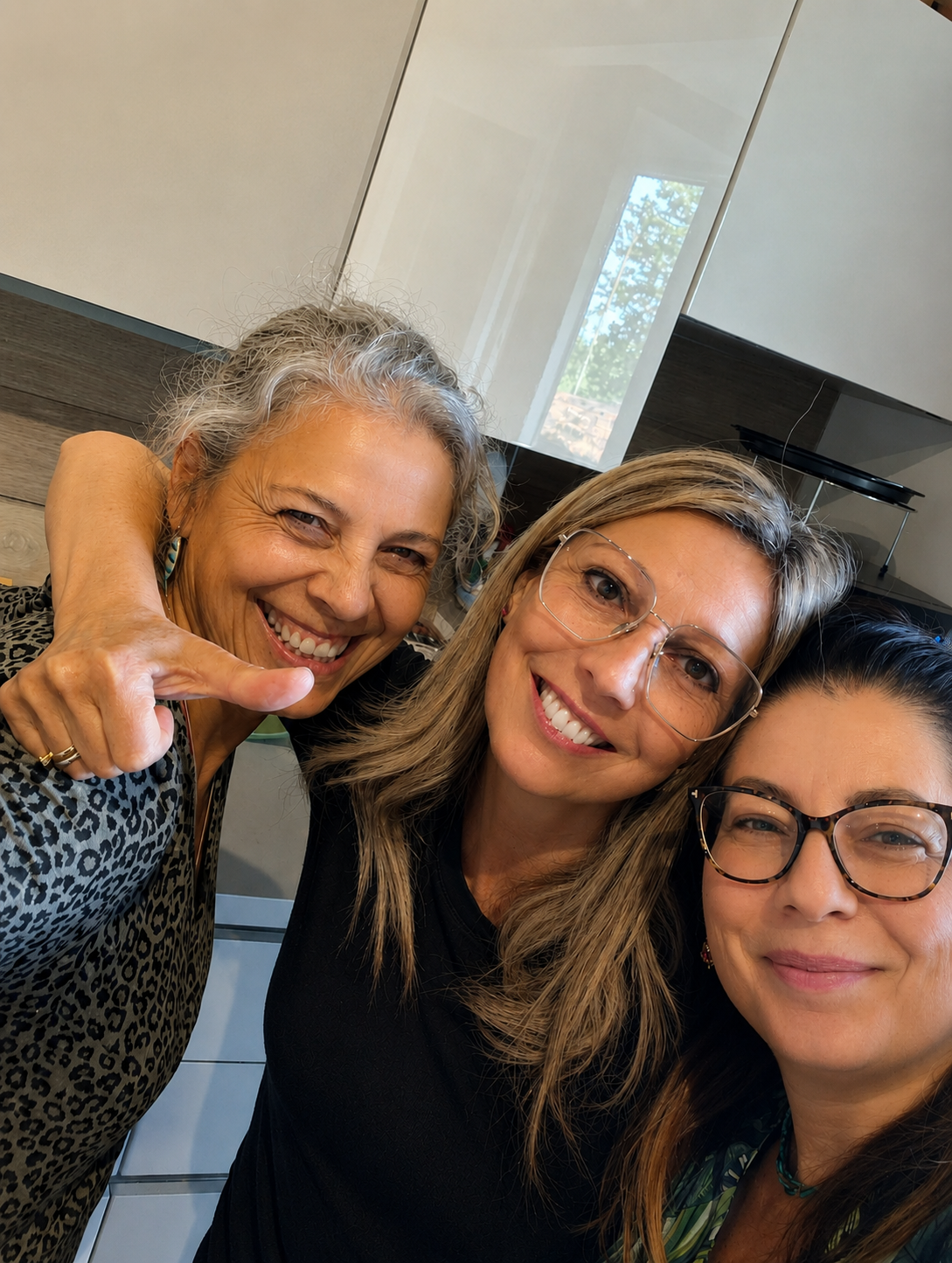 Tre donne sorridenti che si abbracciano e fanno un selfie in cucina.