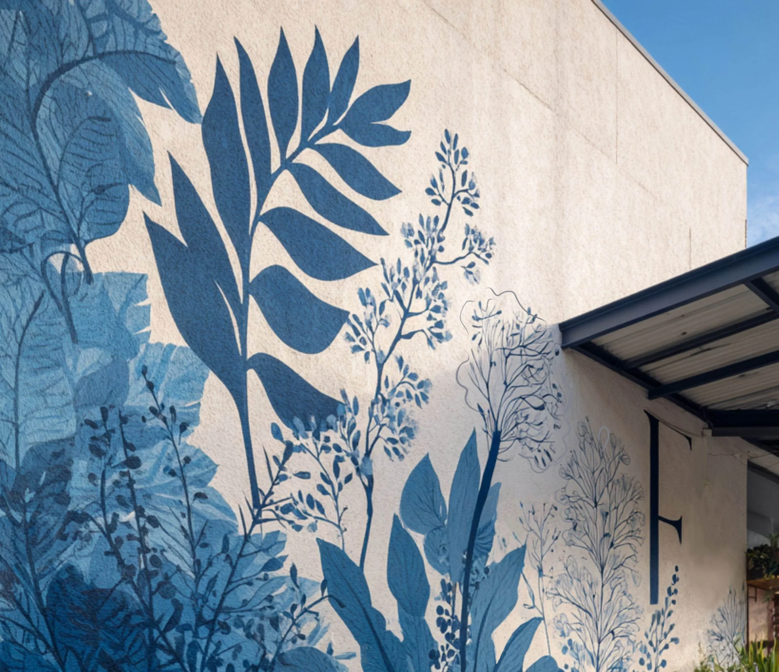 Murale con silhouette di foglie e rami in varie tonalità di blu su una parete beige.