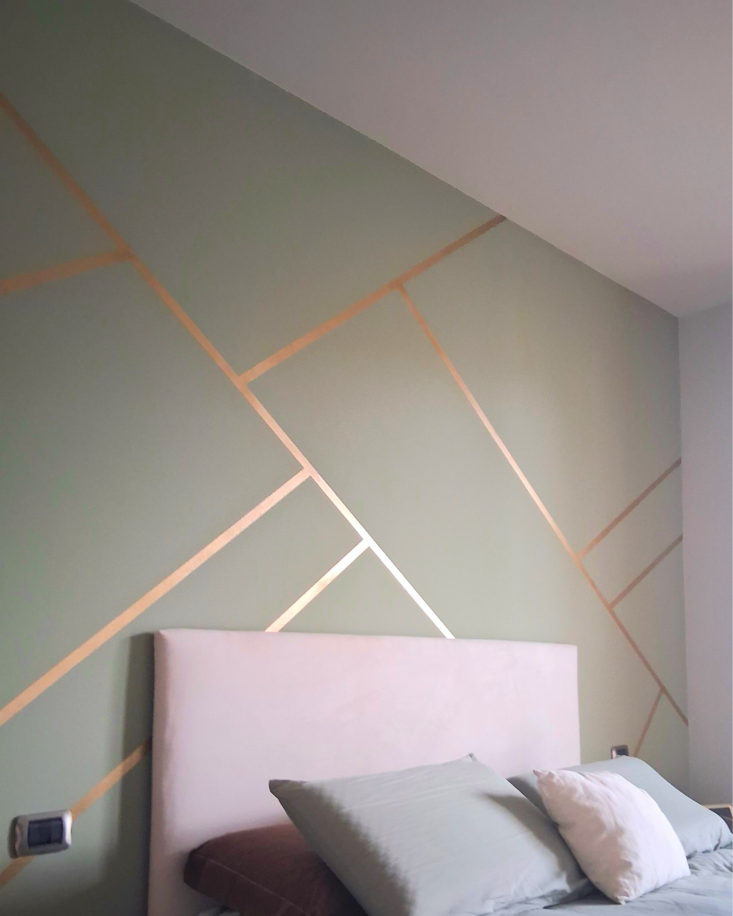Letto matrimoniale con cuscini, parete con decorazioni a linee geometriche in colori pastello.