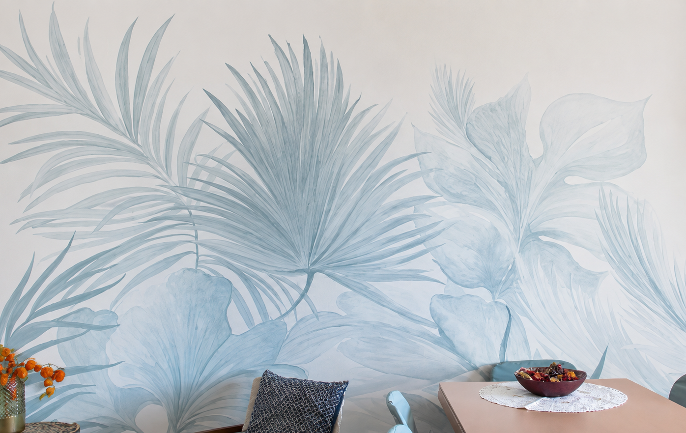 Muro decorato con una grande stampa di foglie di piante tropicali in toni di blu e grigio in un ambiente domestico.
