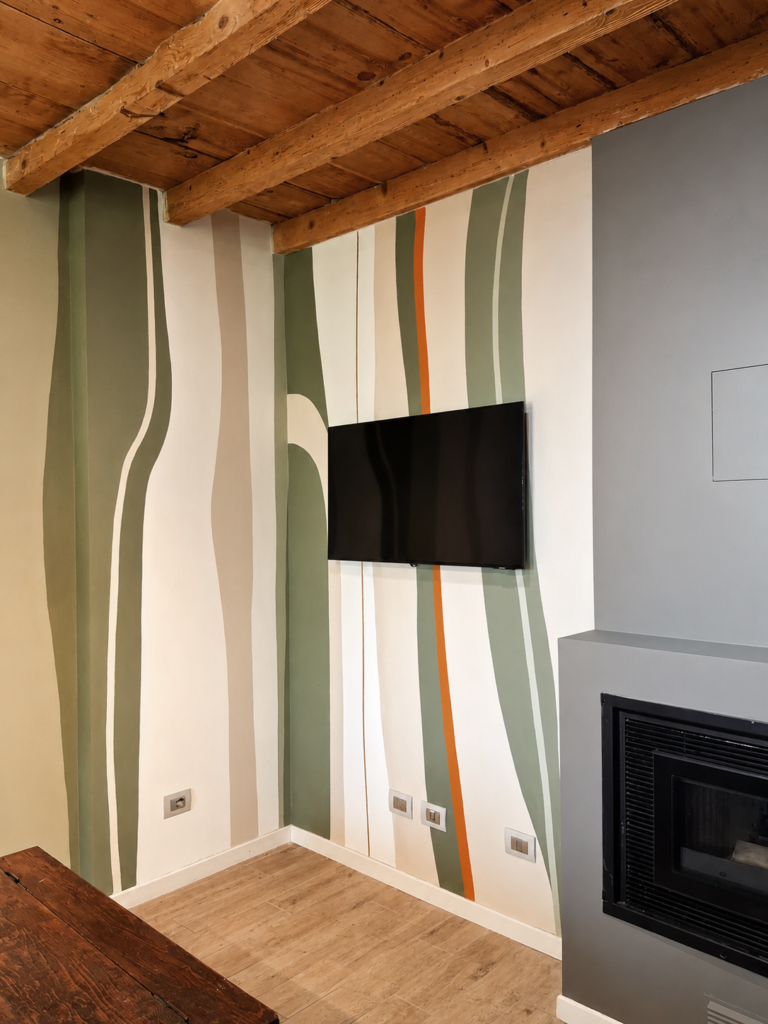 Parete decorata con motivi zigzag verde, beige, e arancione, con un televisore piatto e una stufa a combustione nel soggiorno.