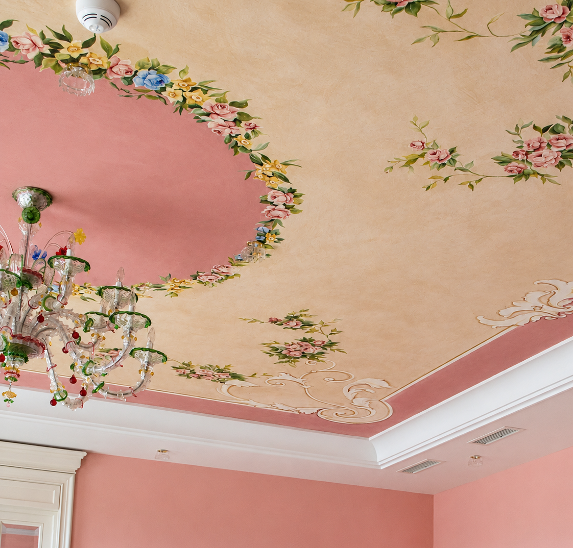 Soffitto decorato con motivi floreali e stucco, lampadario di cristallo colorato, pareti rosa con dettagli bianchi.