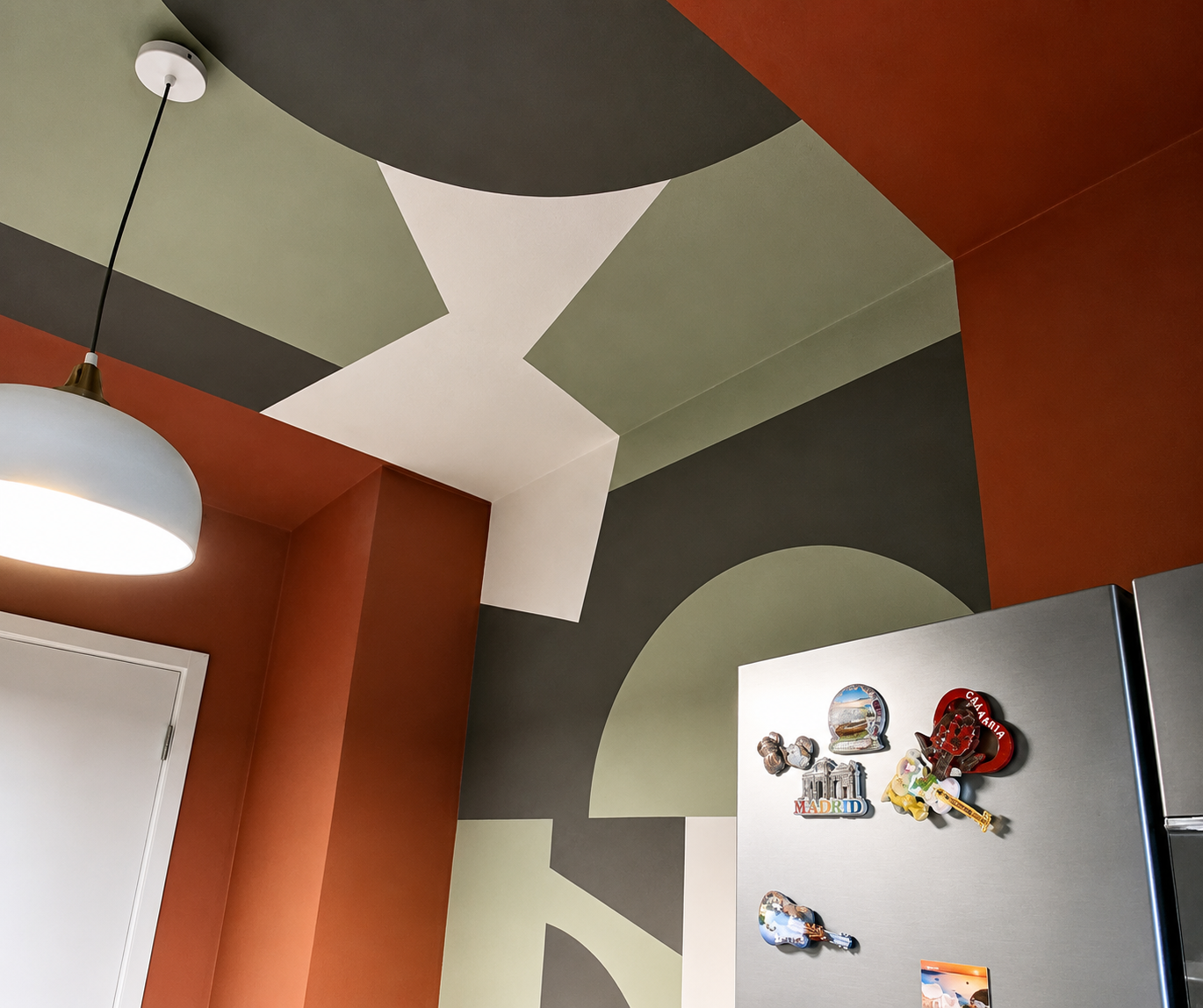 Dettaglio di soffitto e pareti decorati in una cucina moderna con magneti su un frigorifero e una lampada sospesa.