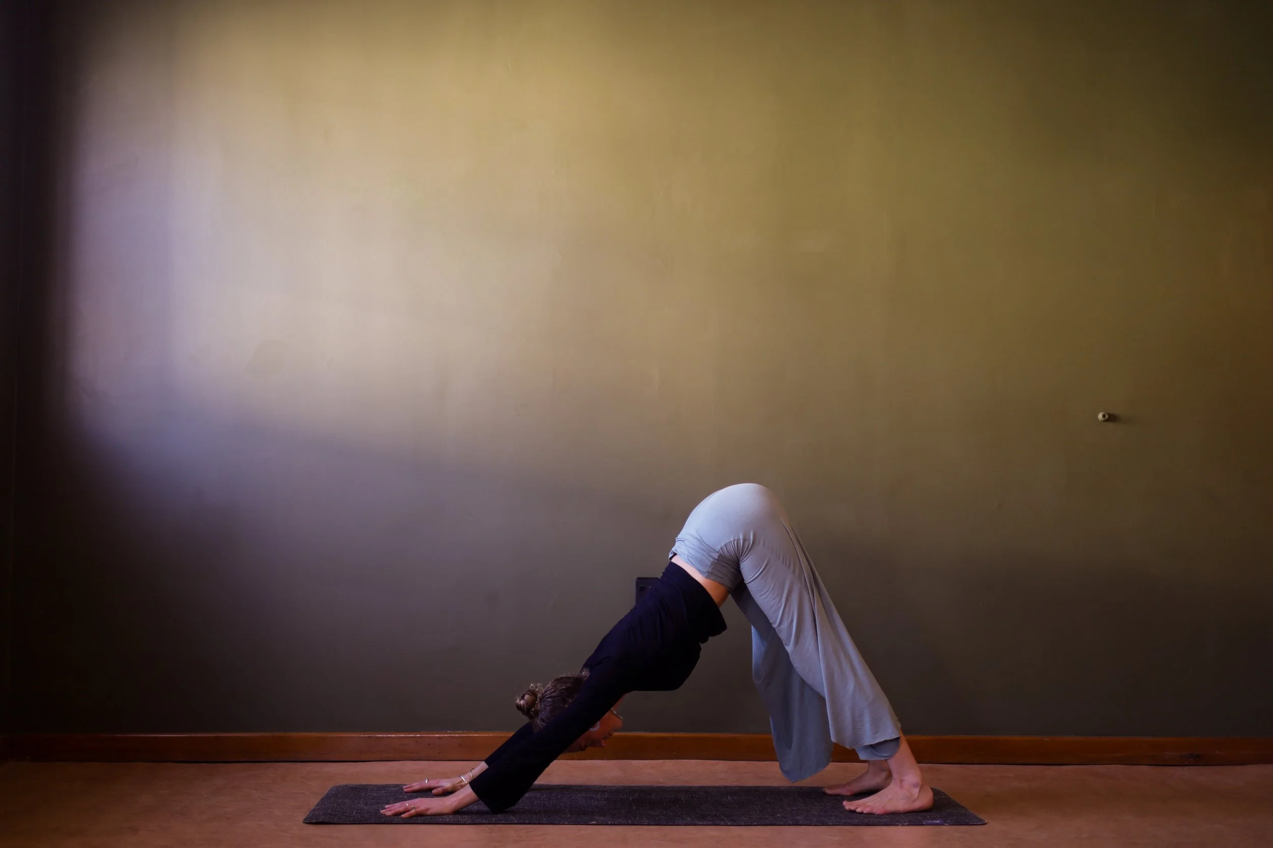 A woman practicing yoga in downward dog pose on a yoga mat in a room with beige walls.