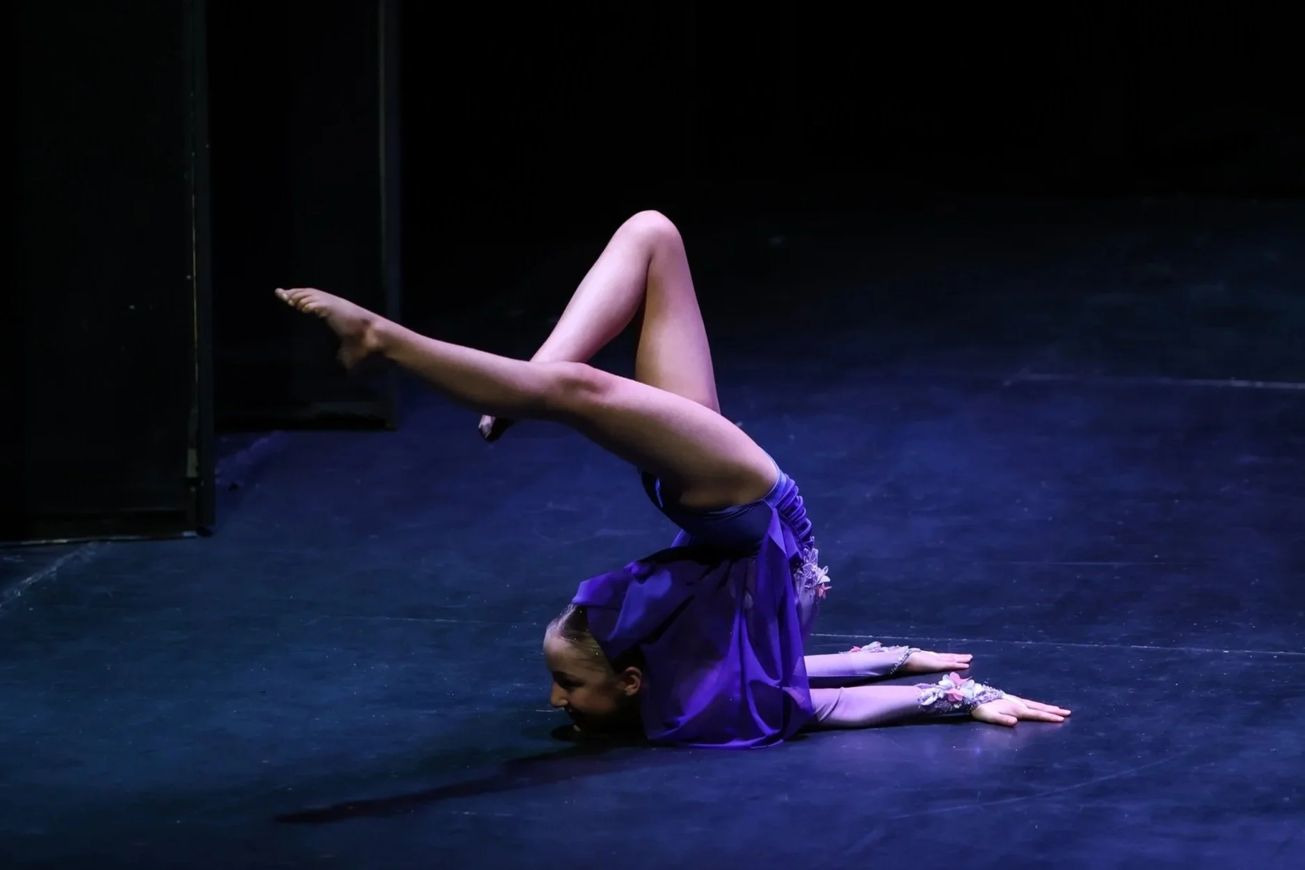 Dancer performing an acro solo, wearing a purple costume.