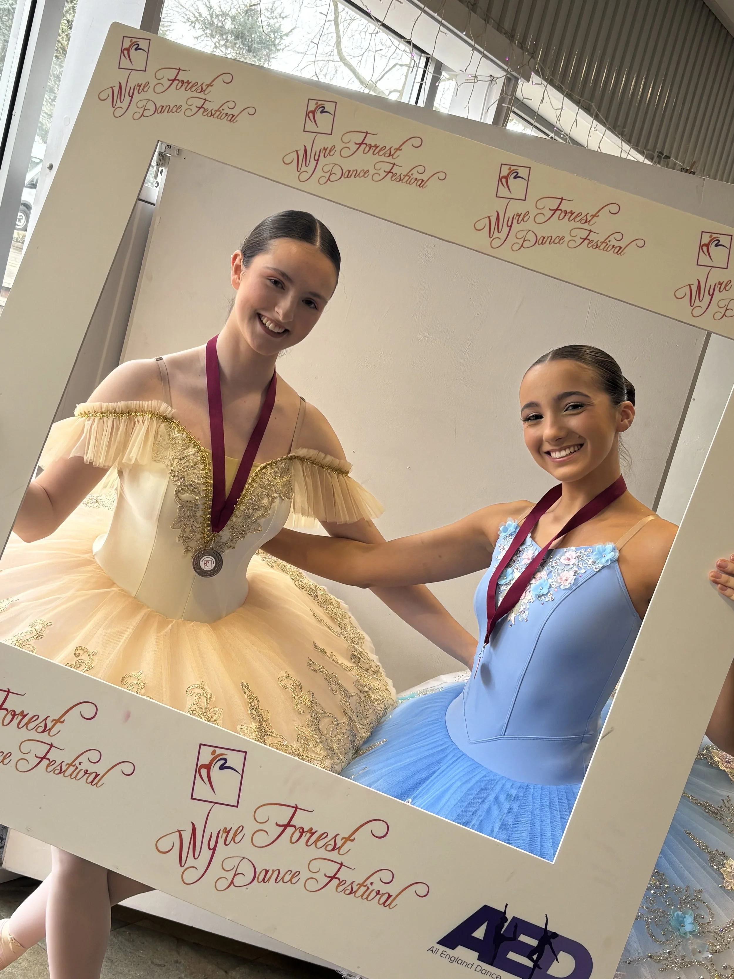 Two young female ballet dancers wearing colourful tutus and medals around their necks pose and smile for a photo at the Wyre Forest Dance Festival.