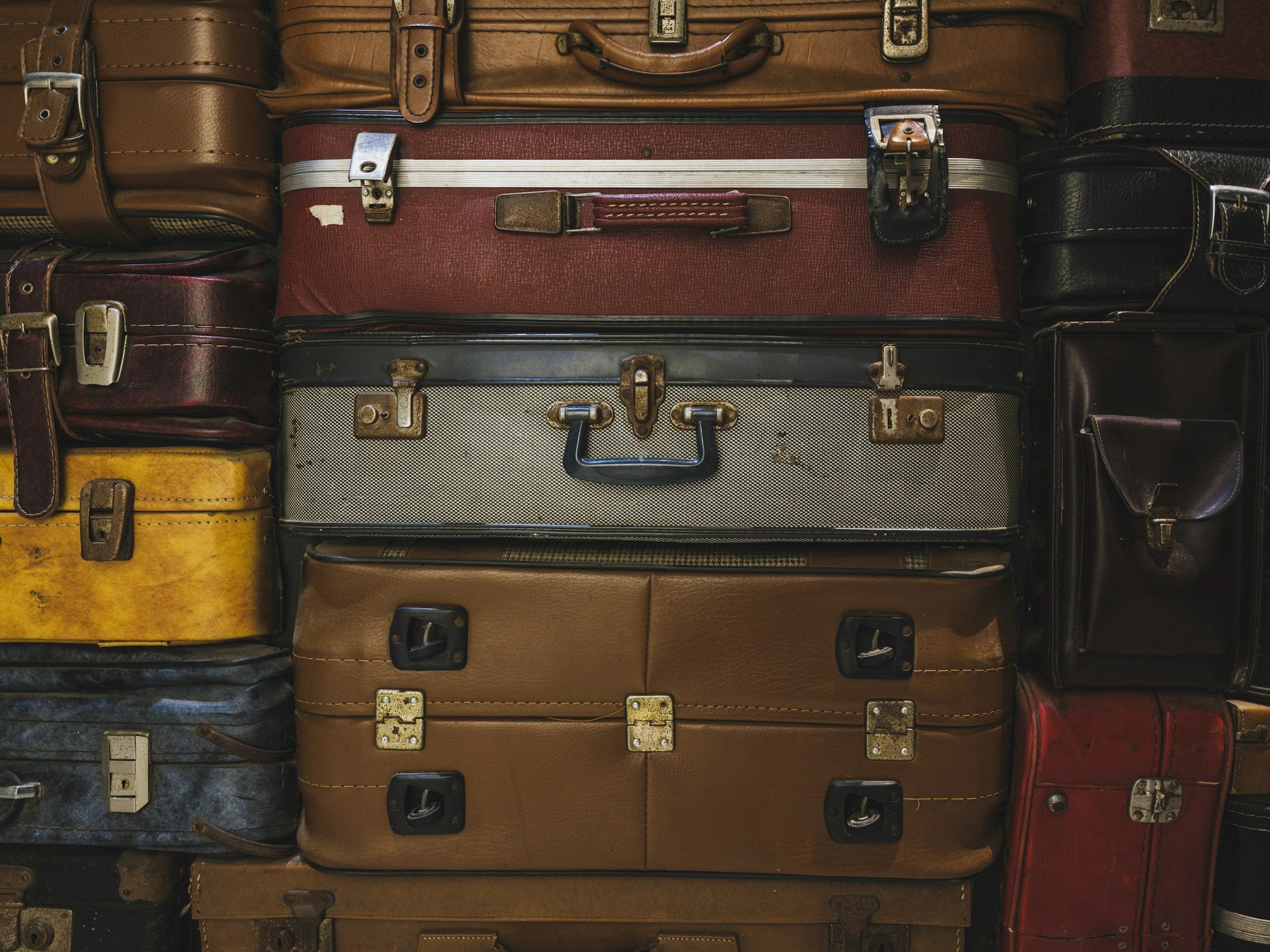 A collection of vintage suitcases stacked together, featuring various colors and sizes with metal clasps and handles.