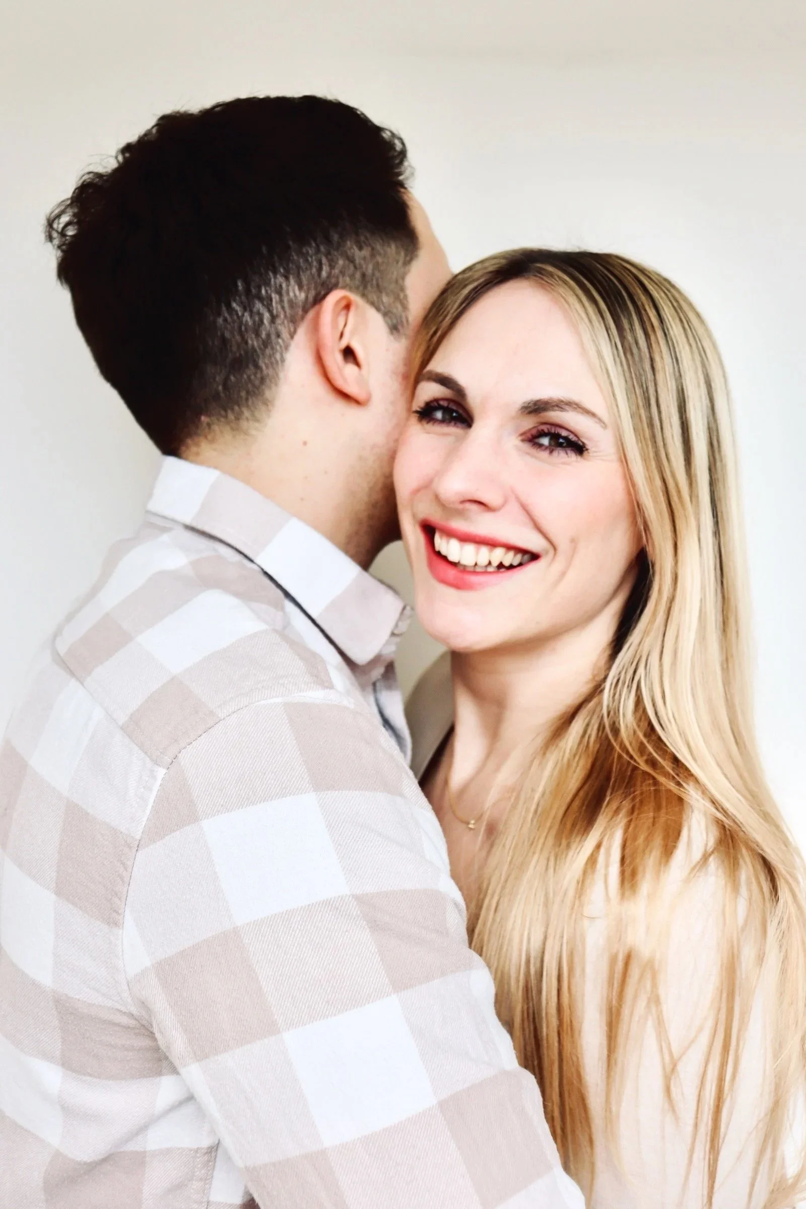 Glückliches Paar, das sich umarmt, während die blonde Frau in die Kamera lächelt, leicht verschwommener Effekt, helle warme Atmosphäre 