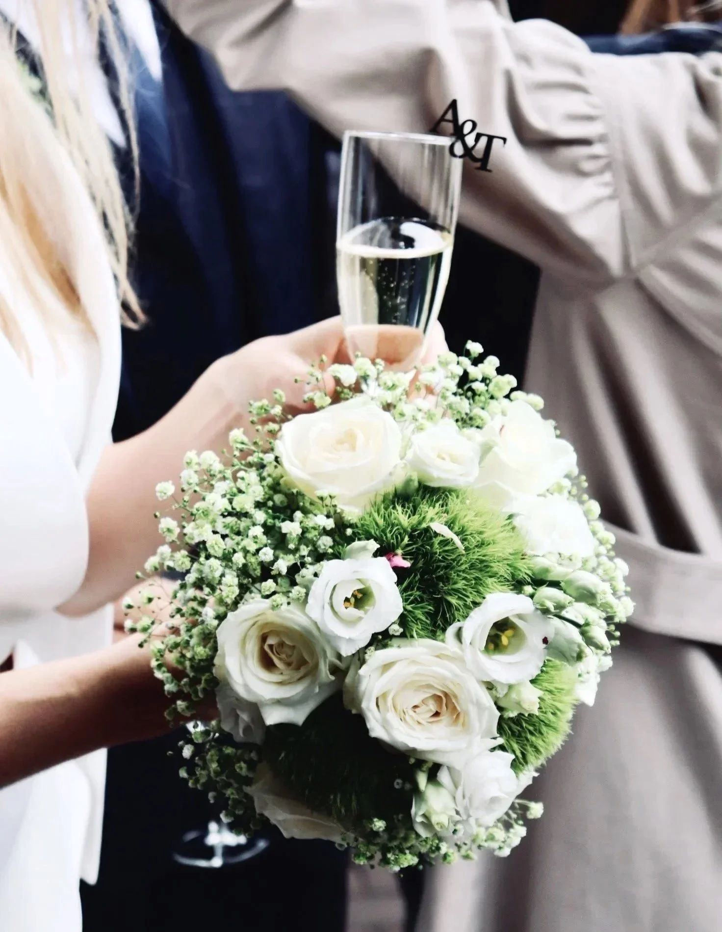 Braut hält einen weißen Blumenstrauß und ein Glas Sekt bei ihrer Hochzeit.