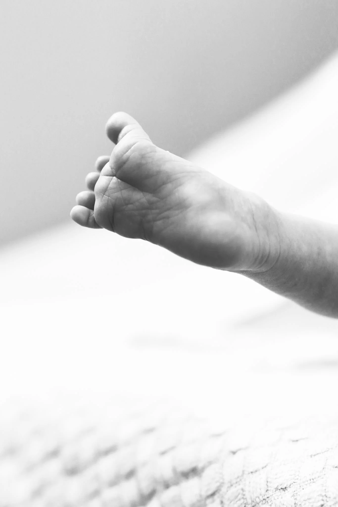 Schwarz-Weiß-Nahaufnahme eines Babyfußes  auf einer hellen Oberfläche, Hintergrund unscharf, Detailaufnahme fokussiert