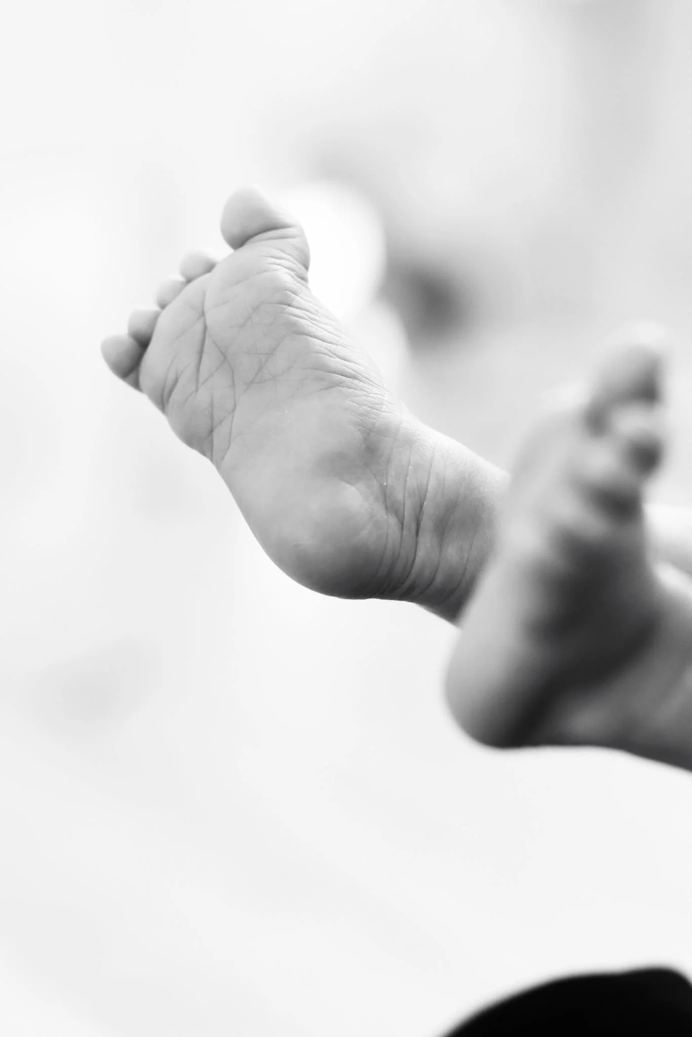 Babyfotografie Nähe Hannover, Bremen, Nienburg und Region, Schwarz-Weiß-Nahaufnahme eines Babyfußes mit sichtbaren Hautfalten, Bokeh-Effekt mit unscharfen Hintergrund und Detailaufnahme des Neugeborenen