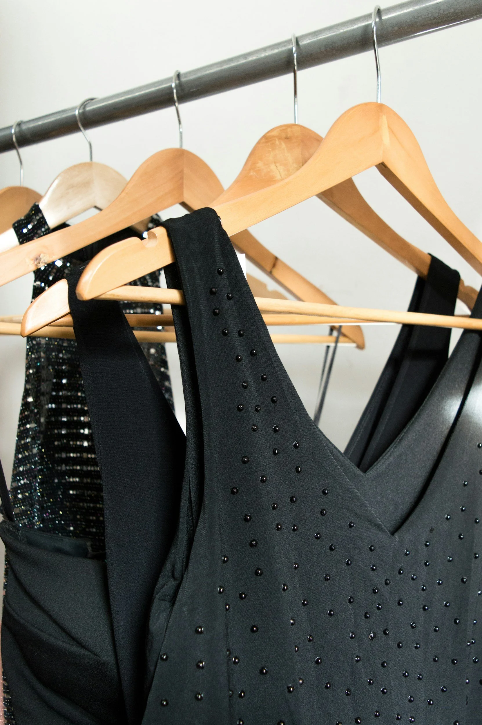 Black dresses with embellishments hanging on wooden hangers on a metal clothing rack.