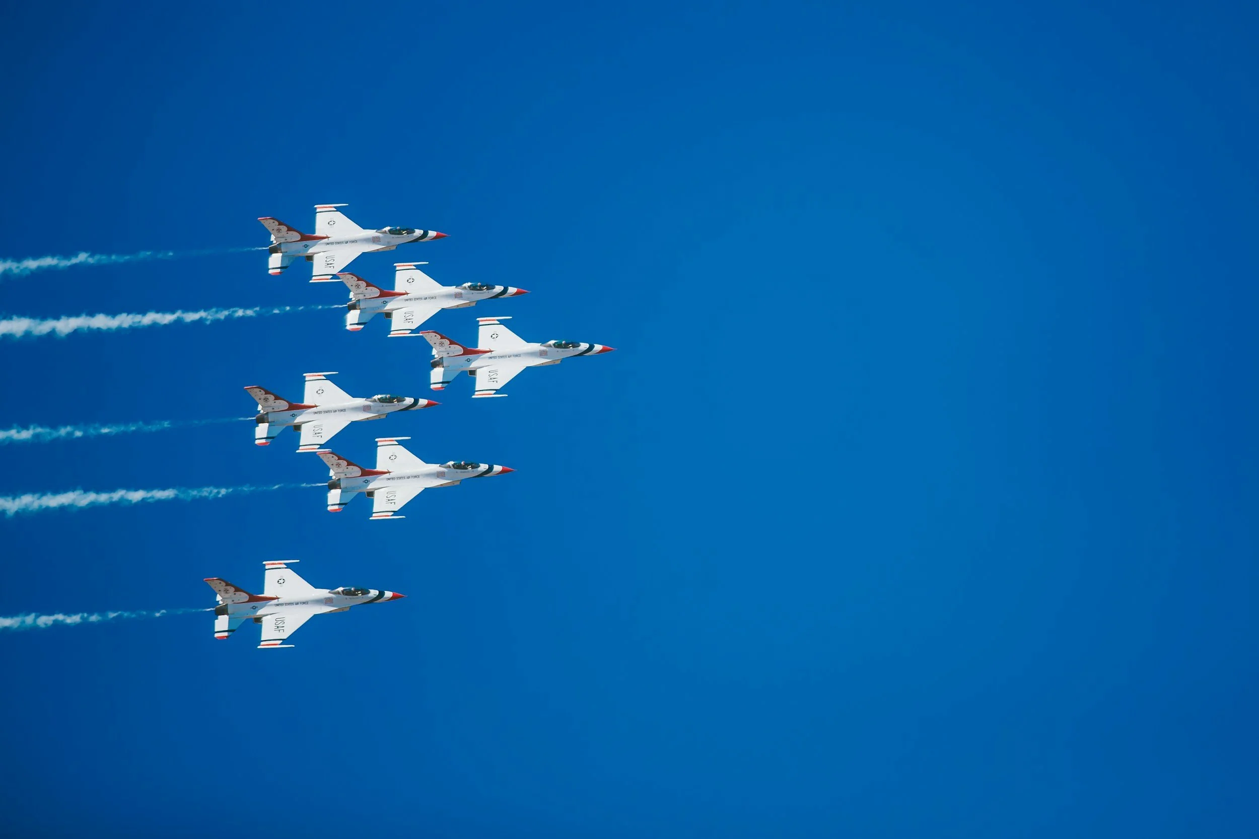 A formation of five fighter jets flying in the sky, leaving white smoke trails behind them against a clear blue sky.