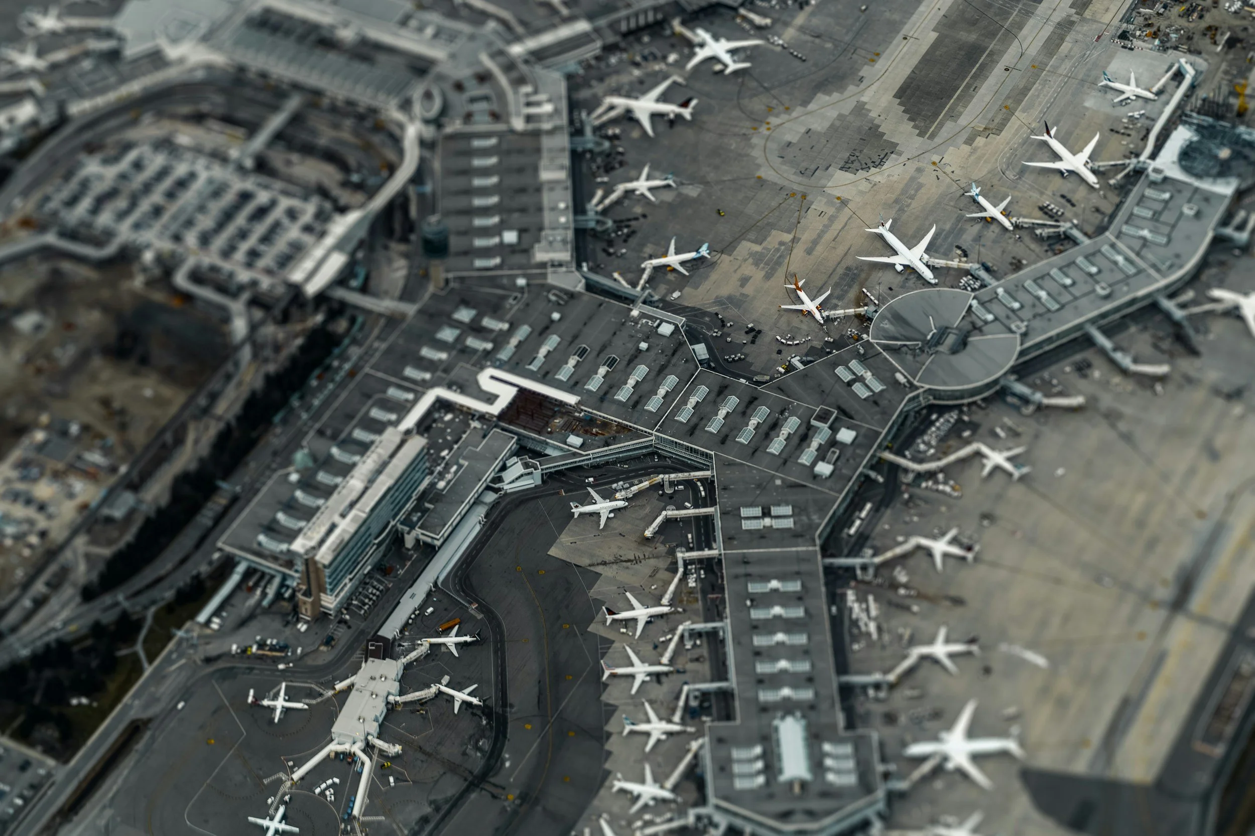 Aerial view of an airport with multiple airplanes parked at gates, connected by jet bridges, and a large terminal building.