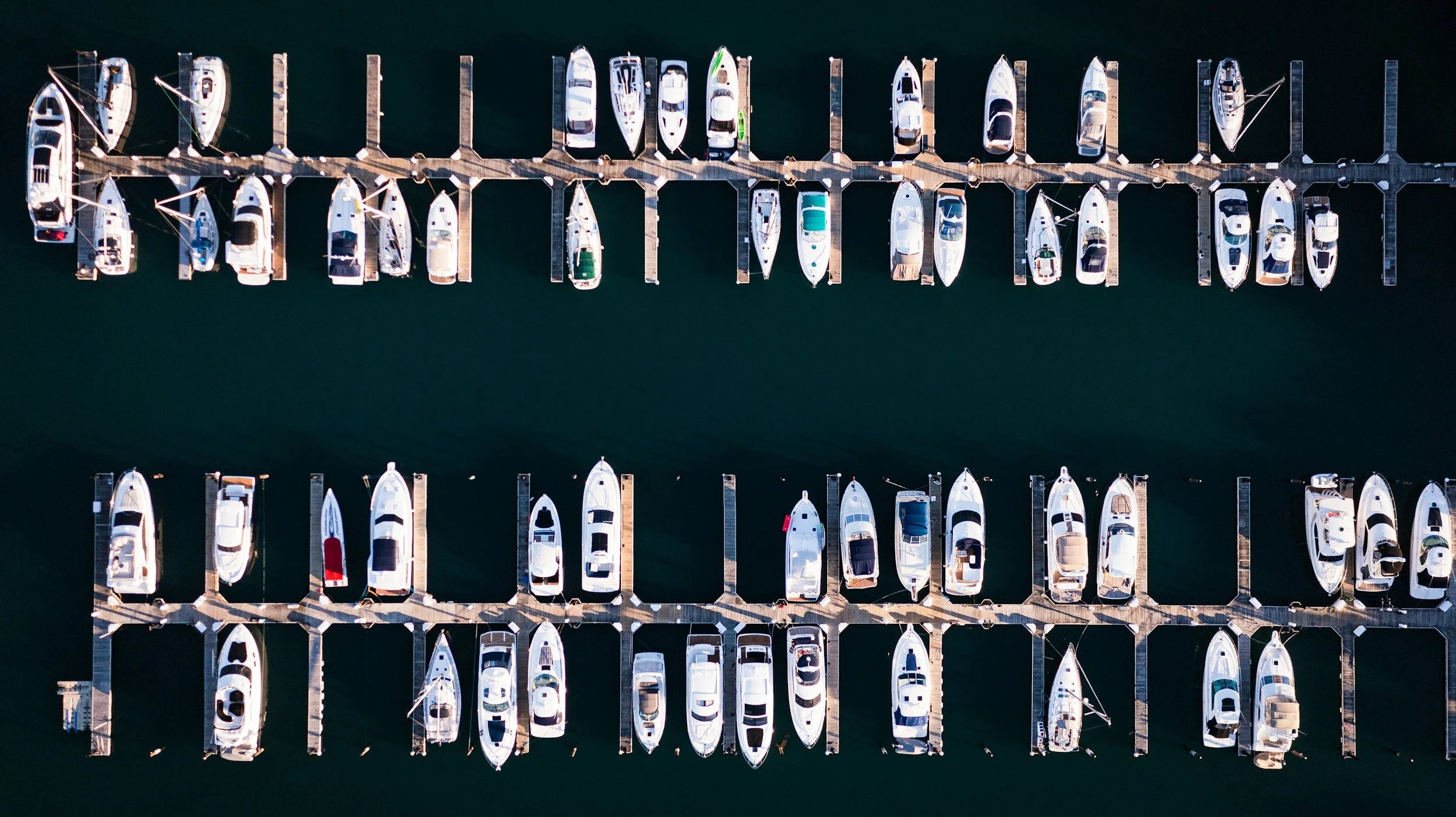 Aerial view of a marina with rows of docked boats and yachts on calm water.