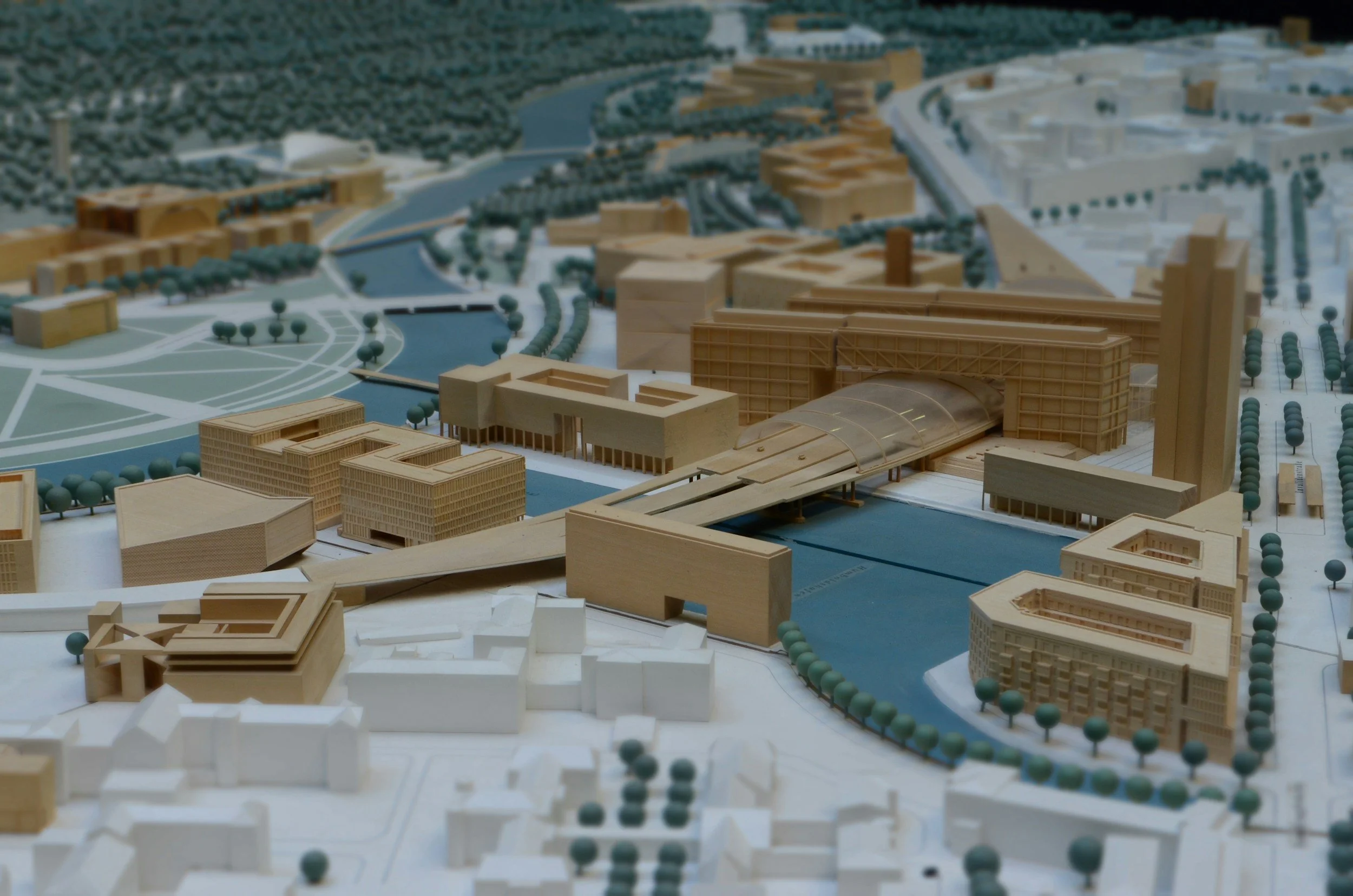 A detailed architectural model of a cityscape featuring various buildings, waterways, and green spaces with trees.