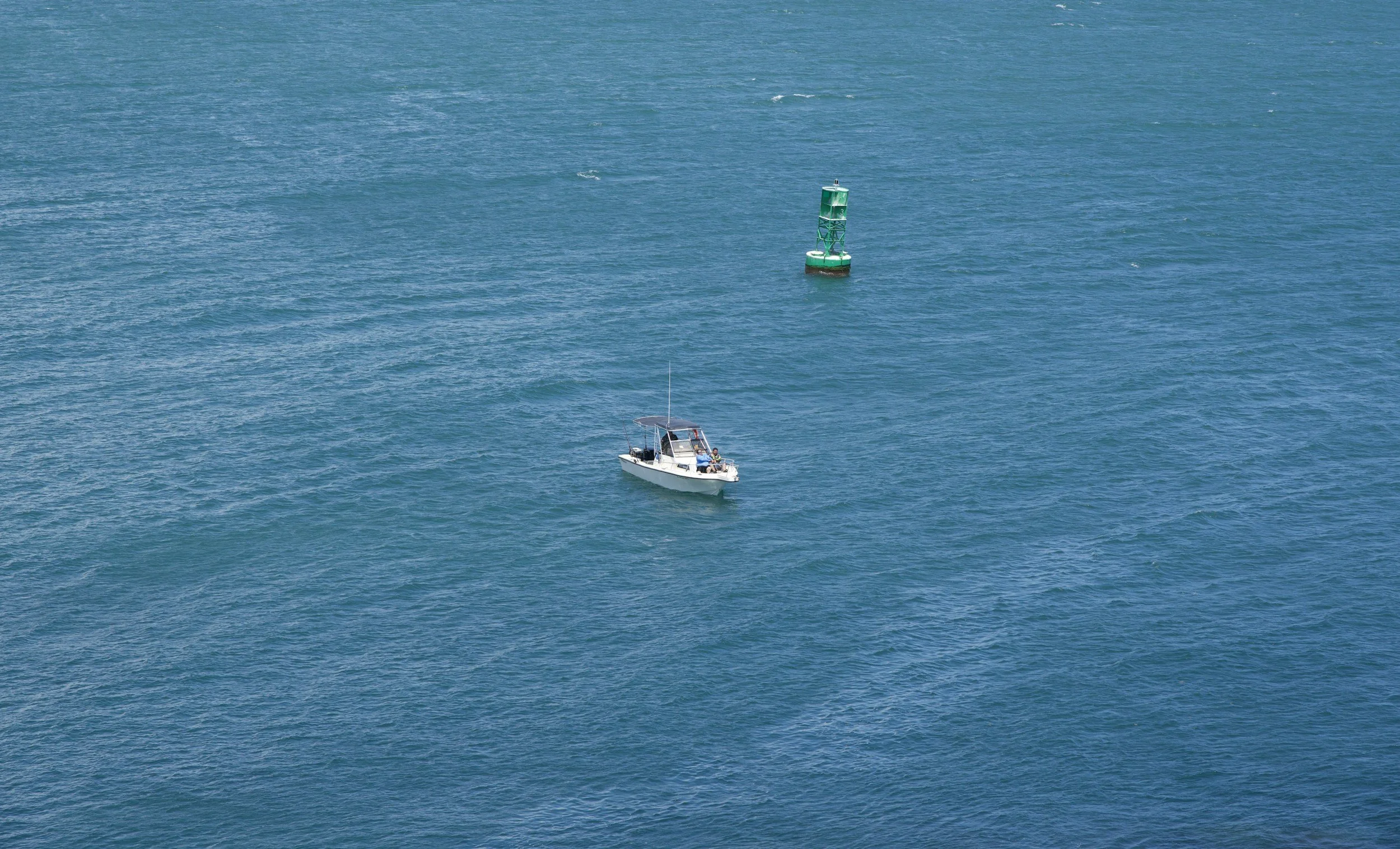 A small white boat with a canopy on blue ocean water, near a green navigation buoy.