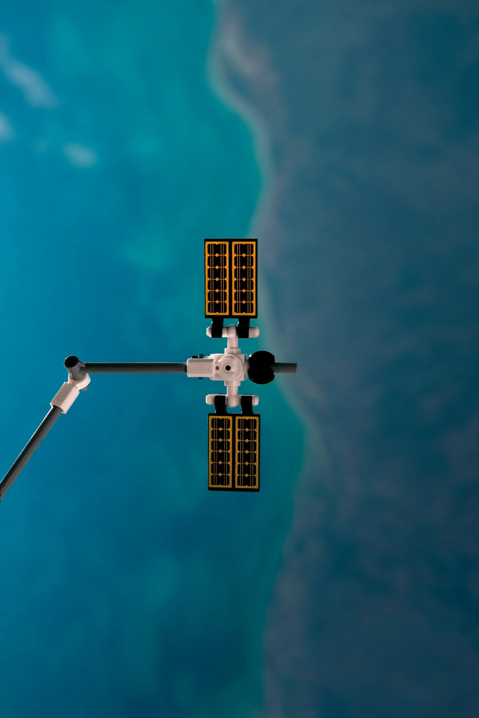 Close-up of a small robotic arm with orange and black solar panels attached, set against a cloudy blue sky.