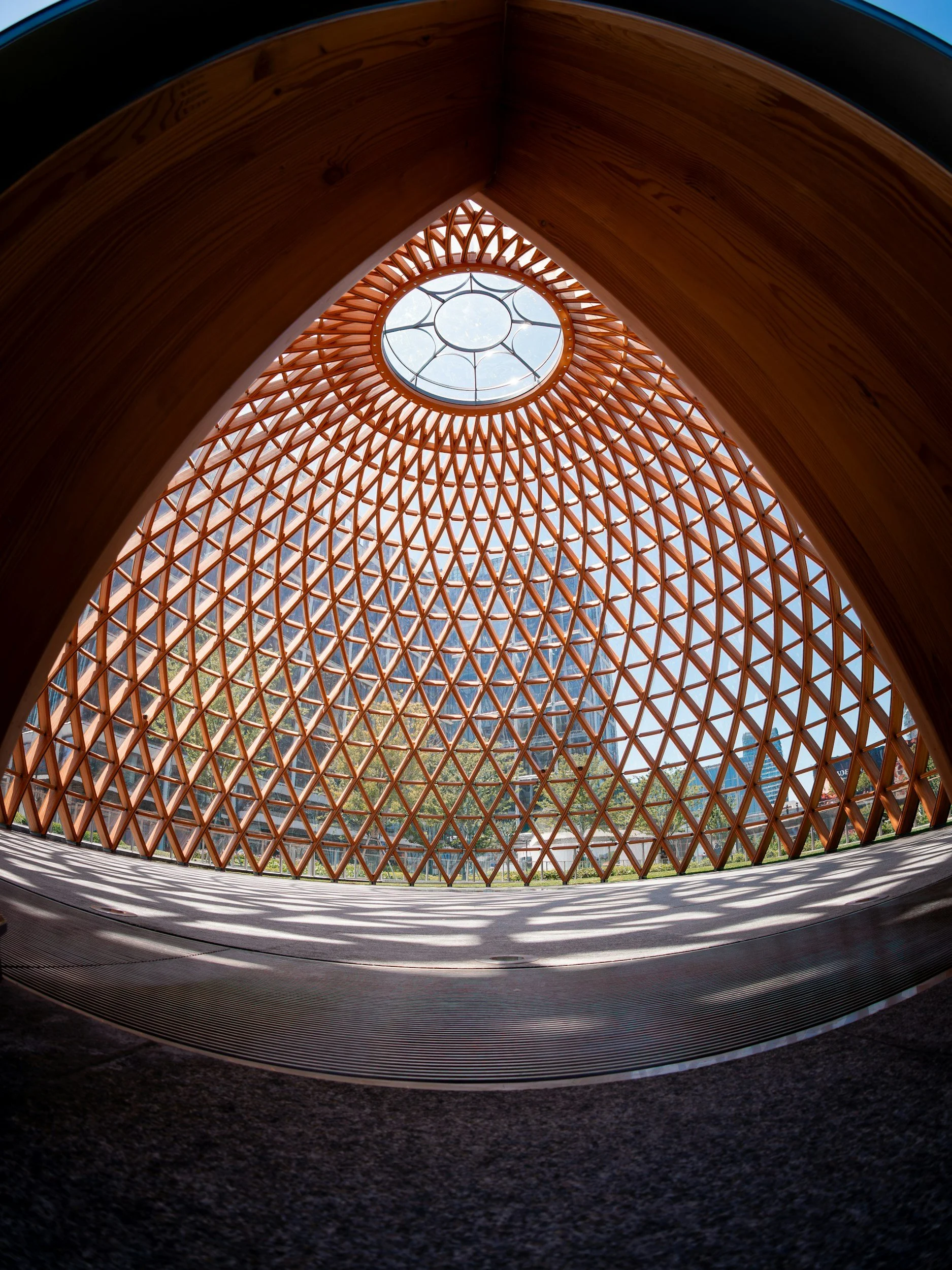 Looking up through a circular, brick lattice dome ceiling with a central skylight, inside a modern building.