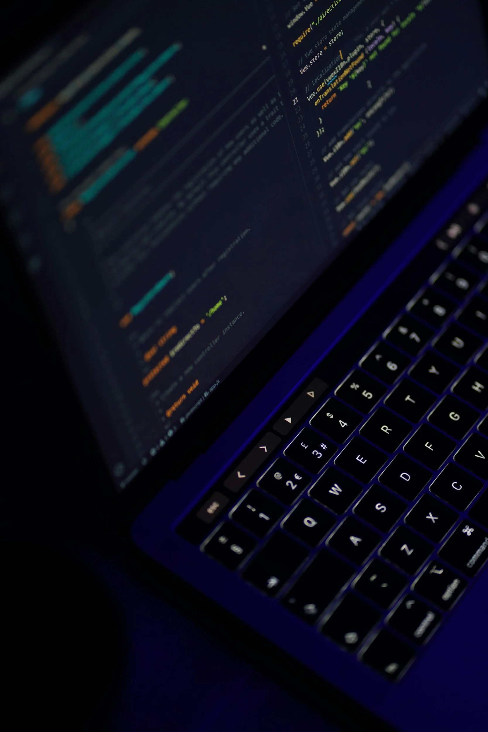 Close-up of a computer screen displaying colorful lines of code in a dark environment, with a portion of a keyboard visible.