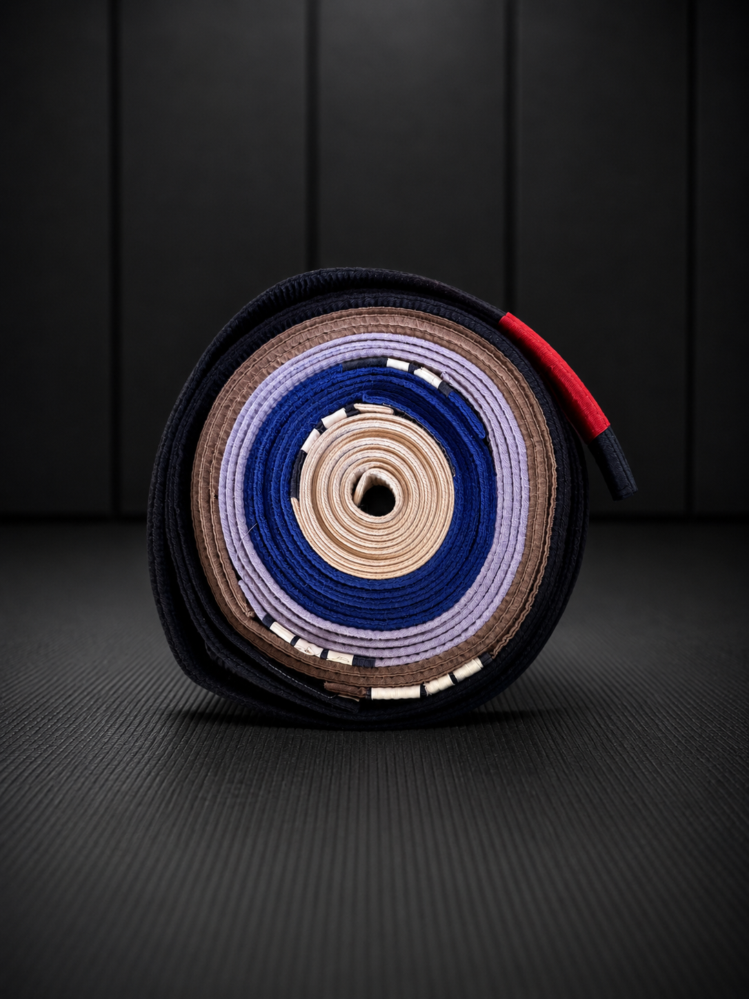 A rolled-up collection of martial arts belts in black, brown, purple, blue, beige, and red, placed on a dark textured surface with a black wooden background.