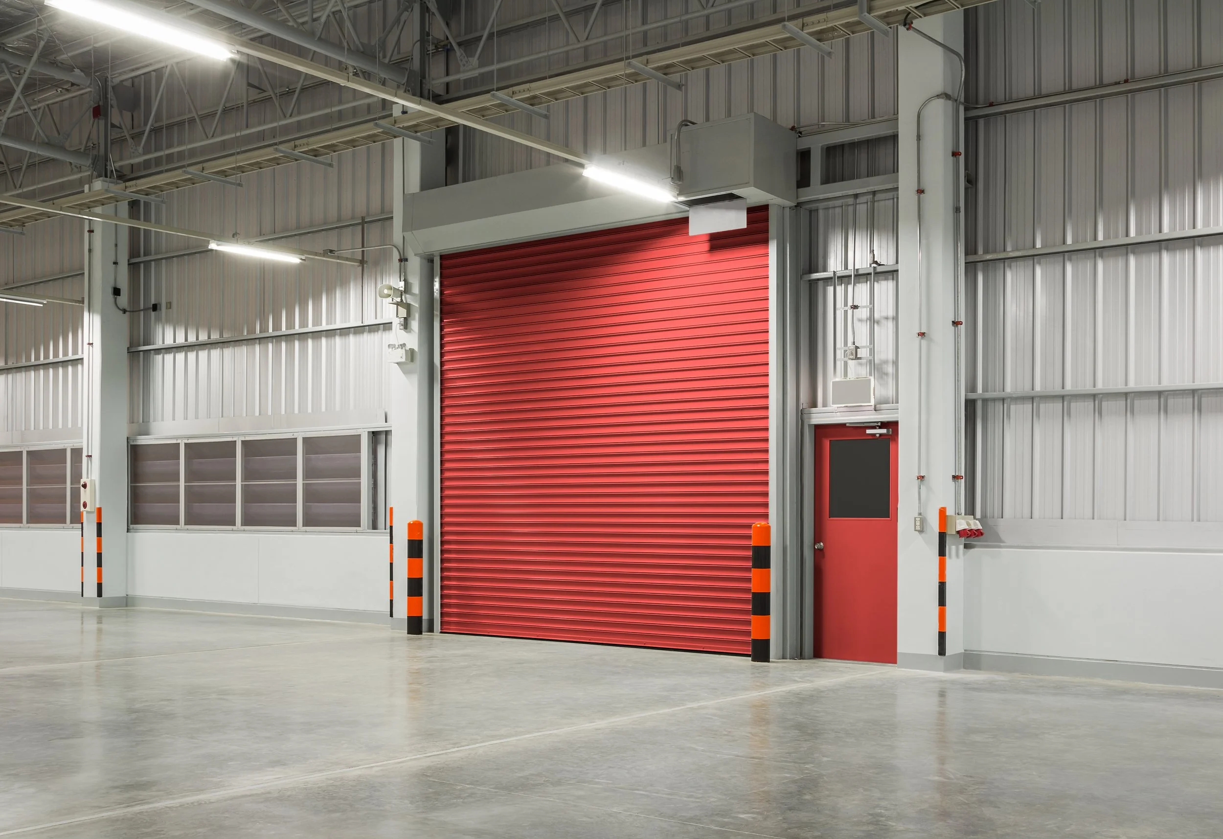 Industrial warehouse with a red roller shutter door, red and black safety bollards.