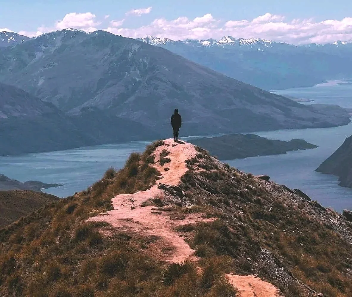 Persoon op een berg met uitzicht op een meer wat staat voor een kalme staat voor innerlijke wonden helen en gaven herinneren