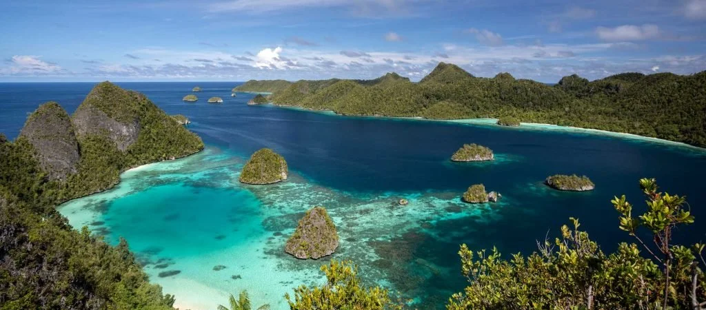 Aerial view of a tropical island with lush green mountains, turquoise waters, and small islands in the bay.
