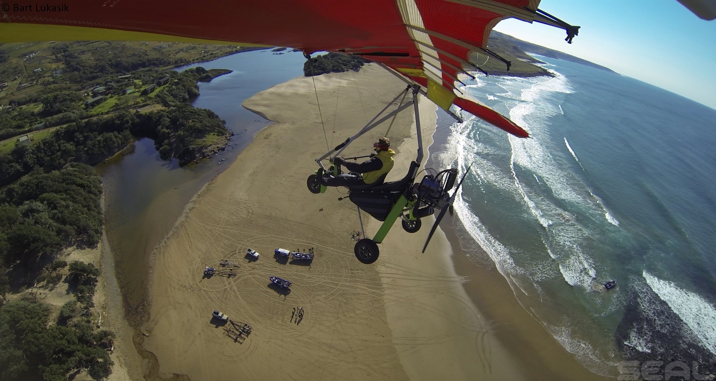 A person flying a microlight aircraft over a beach and coastal landscape during daytime.