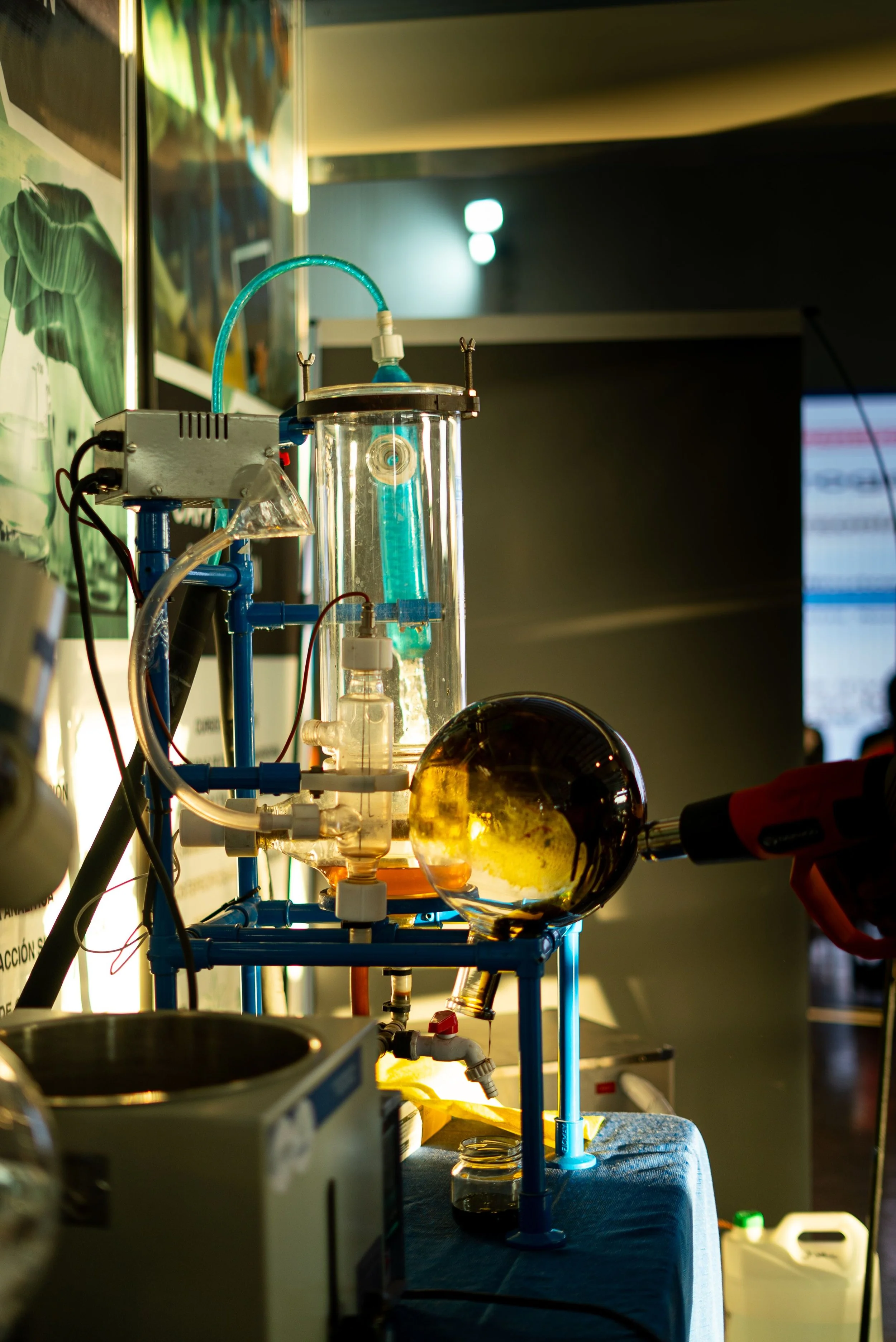 Laboratory setup with glassware, tubes, and equipment, with a glowing yellow substance in a spherical glass vessel, illuminated by a light source.