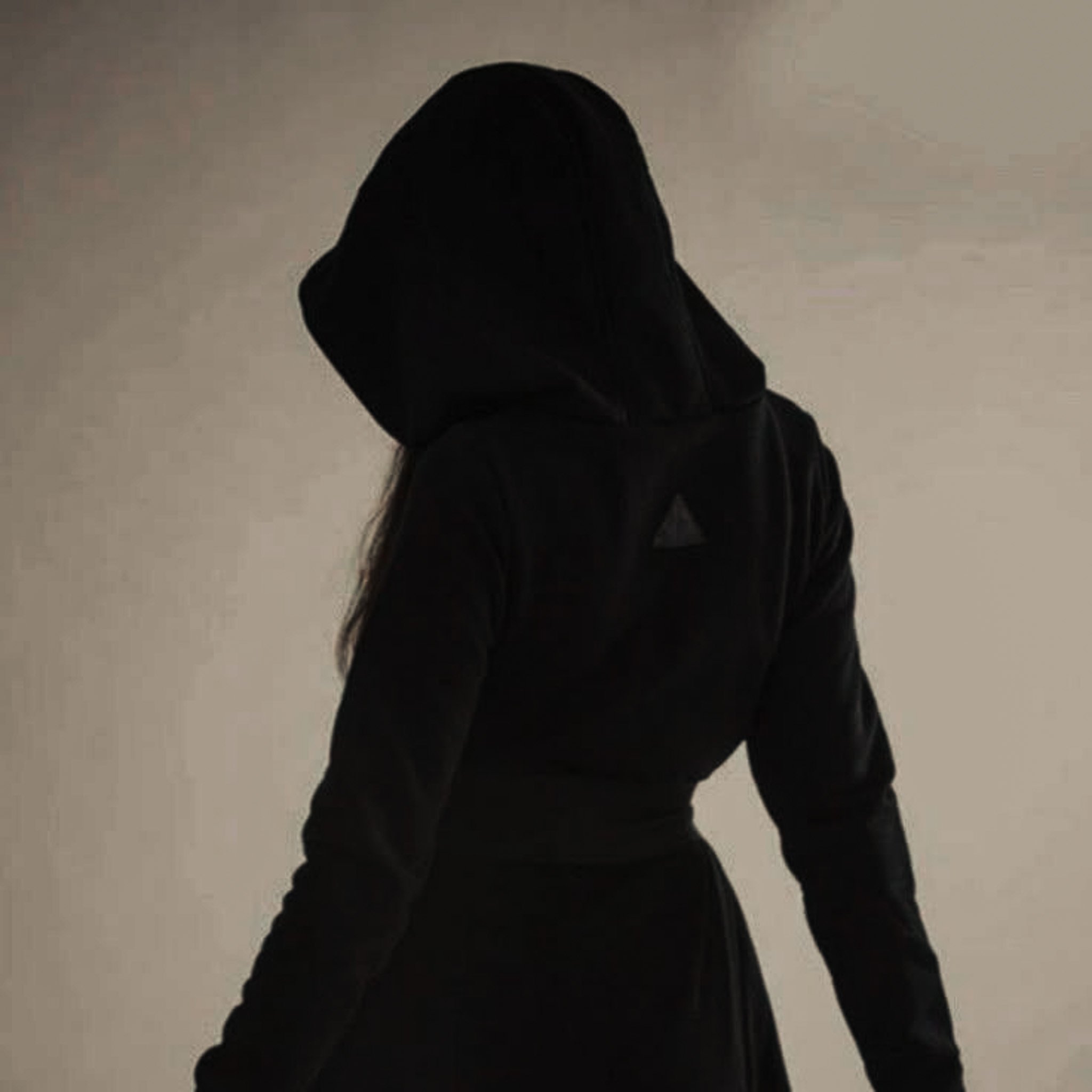 Silhouette of a person wearing a hoodie, facing sideways in a dimly lit environment.